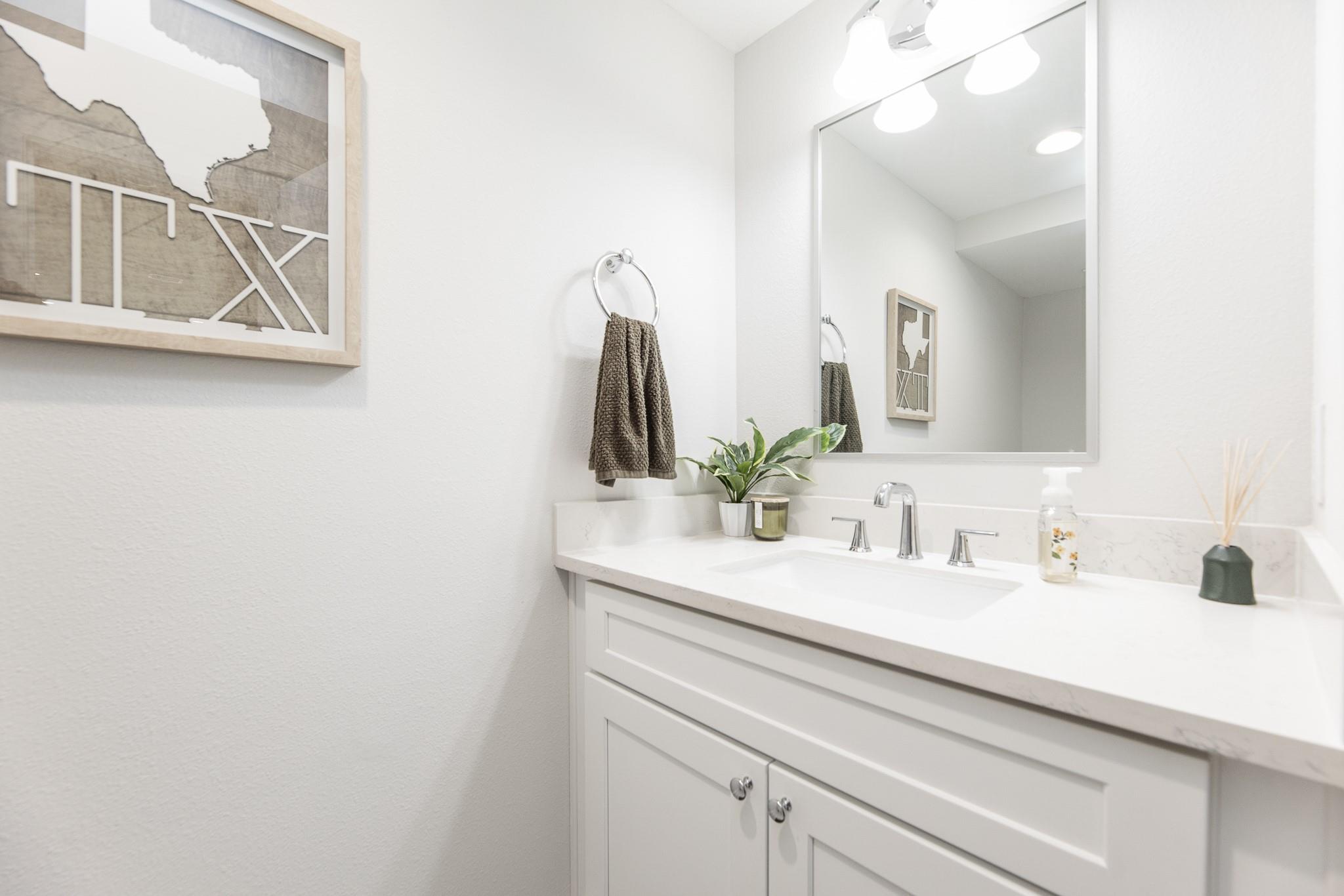 Bathroom vanity with a white countertop, chrome fixtures, and framed Texas artwork.