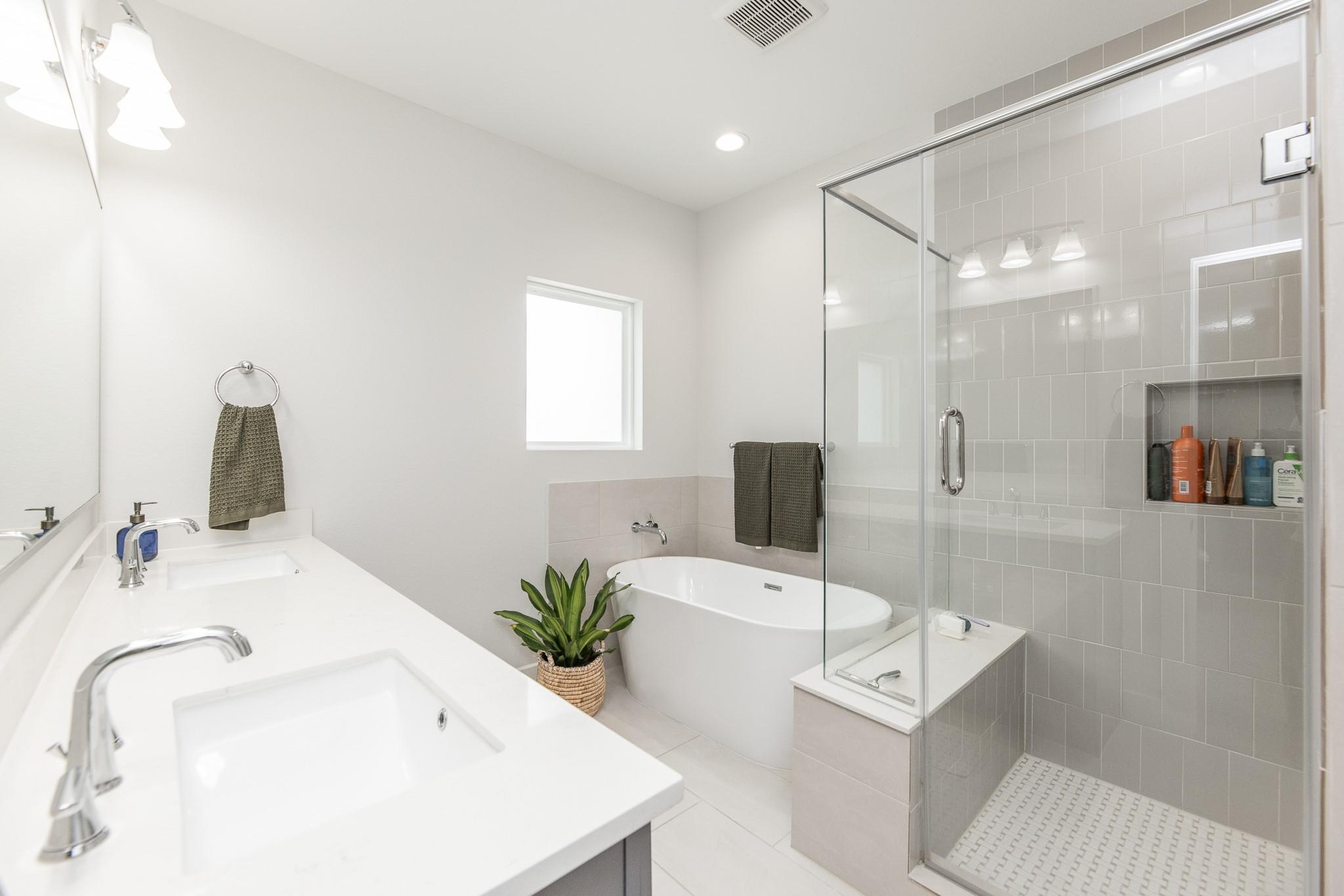 Bathroom with double-sink vanity, freestanding tub, and gray-tiled glass shower.