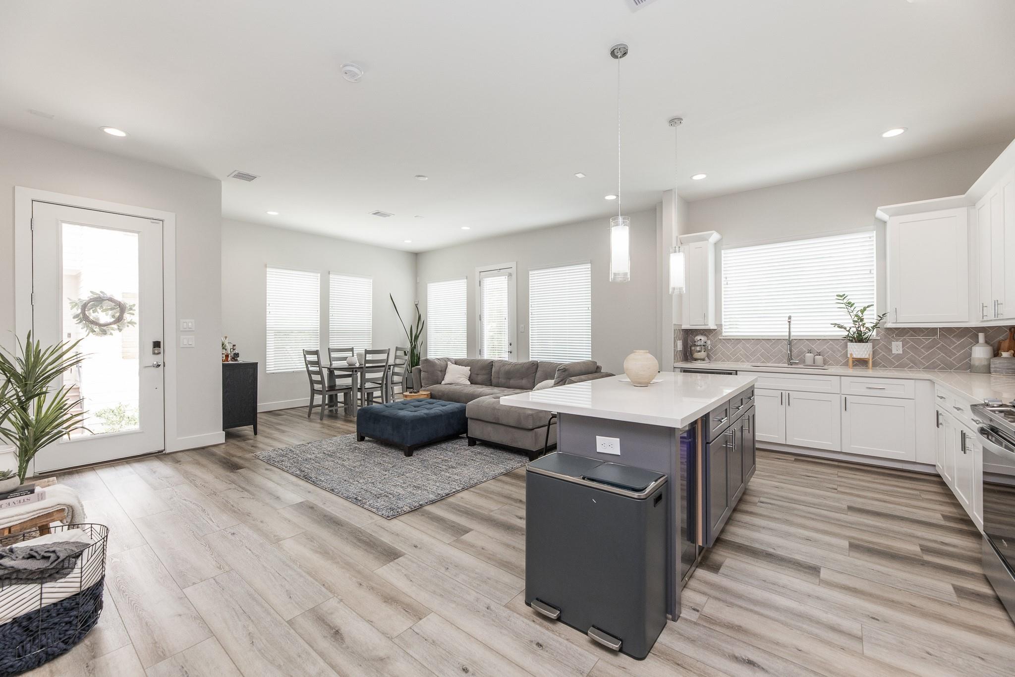 Open-plan kitchen and living room with a large island, gray sectional, and bright windows.