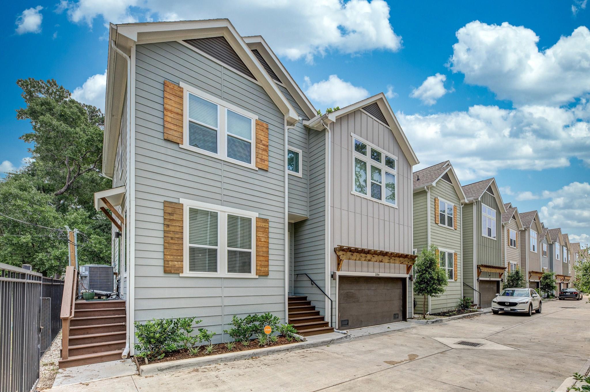 Gray two-story townhouse with a garage, wood shutters, and neighboring homes along a shared driveway.