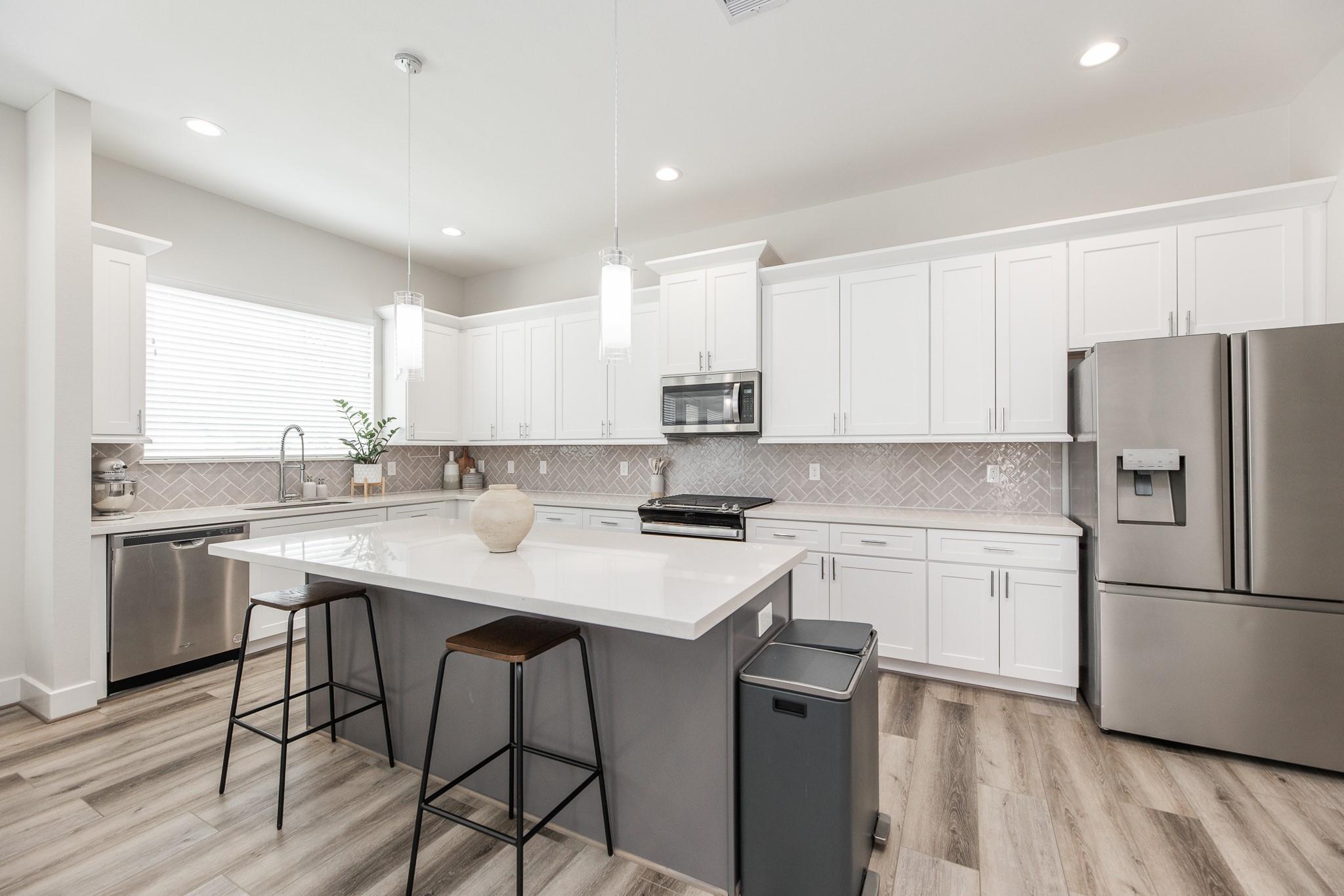 Modern kitchen with a gray island, white cabinets, stainless appliances, and herringbone backsplash.