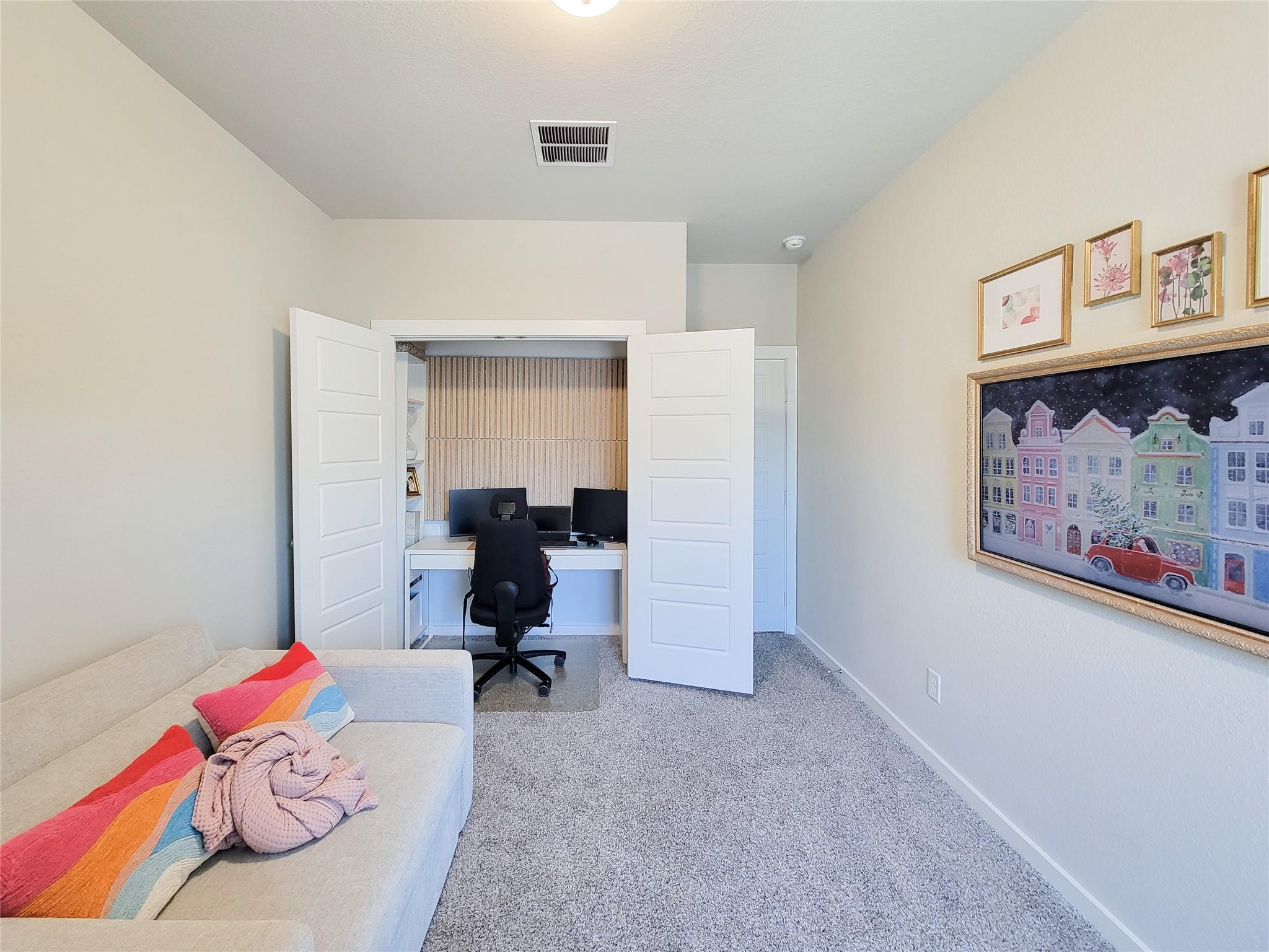Carpeted room with a desk and office chair in an open-door alcove beside a sofa.