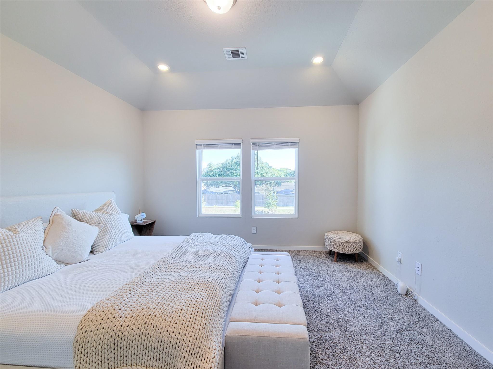 Staged bedroom with white bedding, a chunky knit blanket, and two windows.