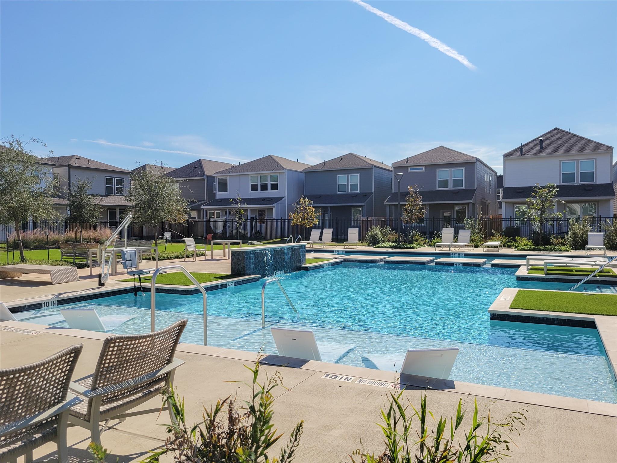 Community pool with shallow tanning ledges, lounge chairs, and two-story homes in the background.