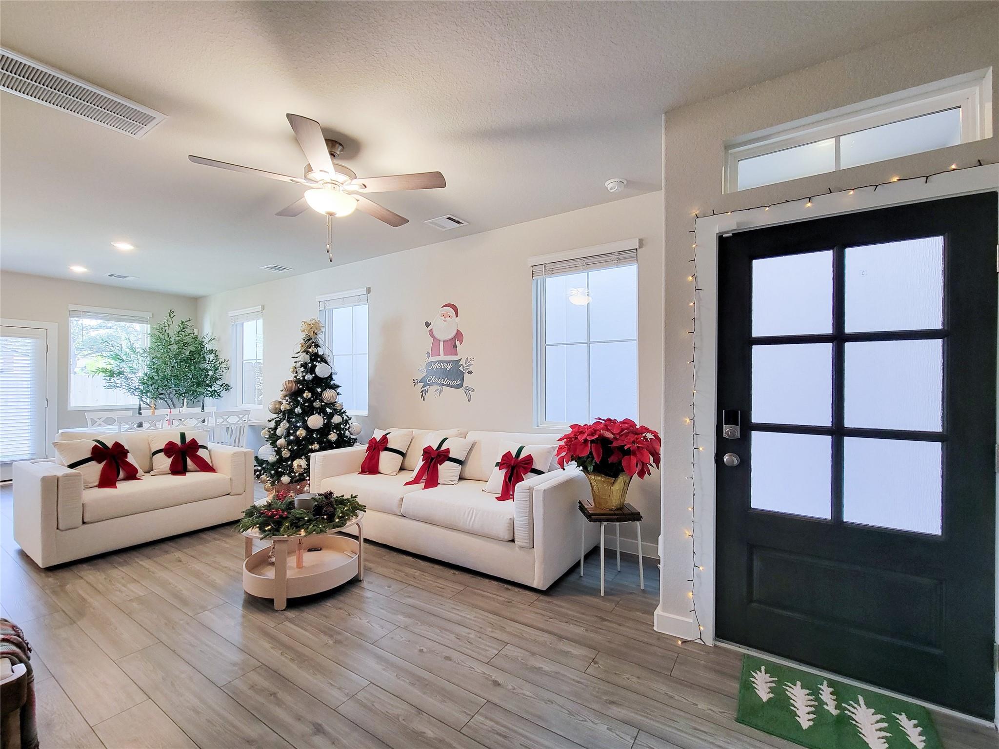 Living room with white sofas, a decorated Christmas tree, and a black front door edged with lights.