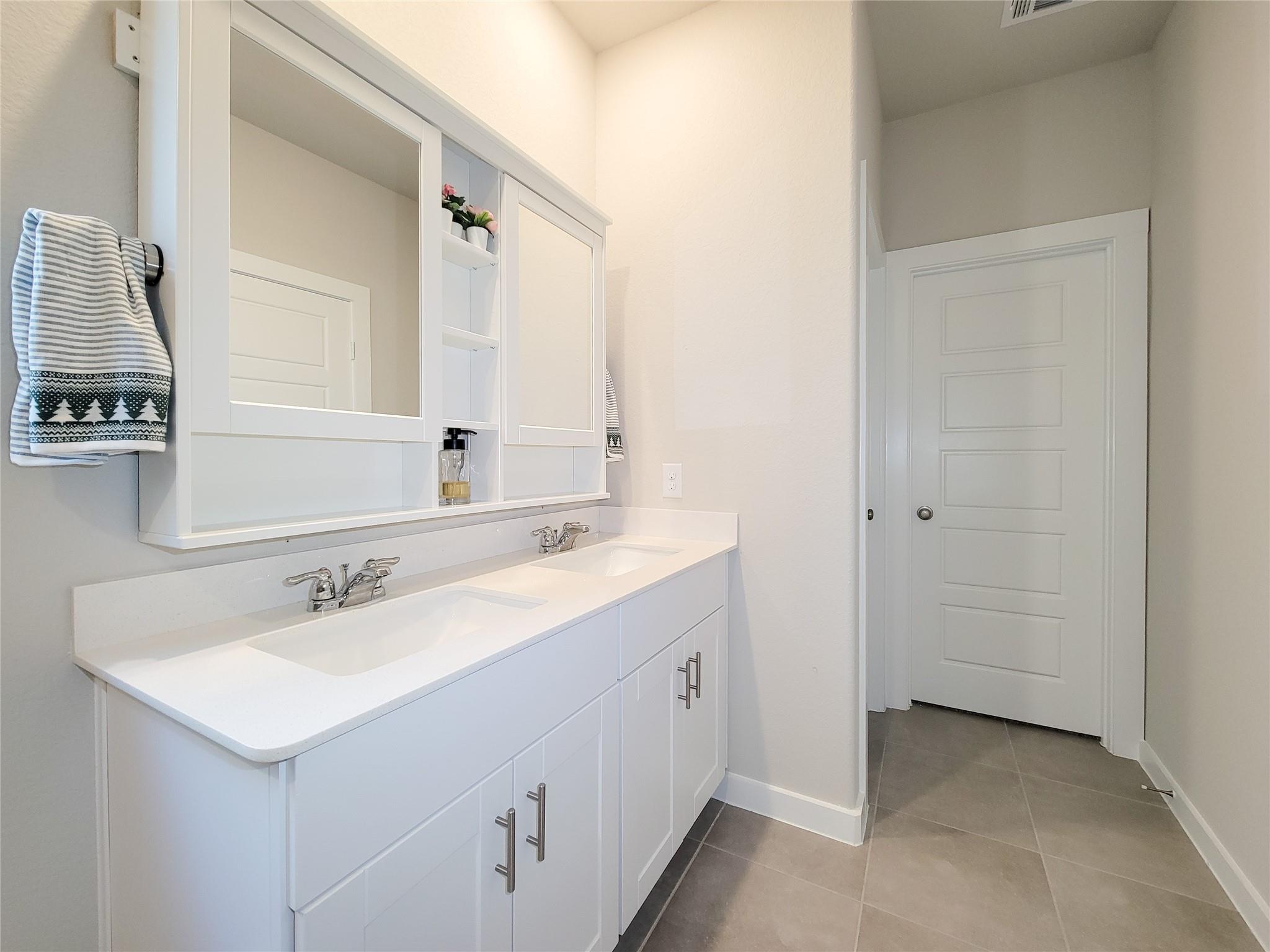 Bathroom with a white double-sink vanity, mirrored storage, and gray tile flooring.