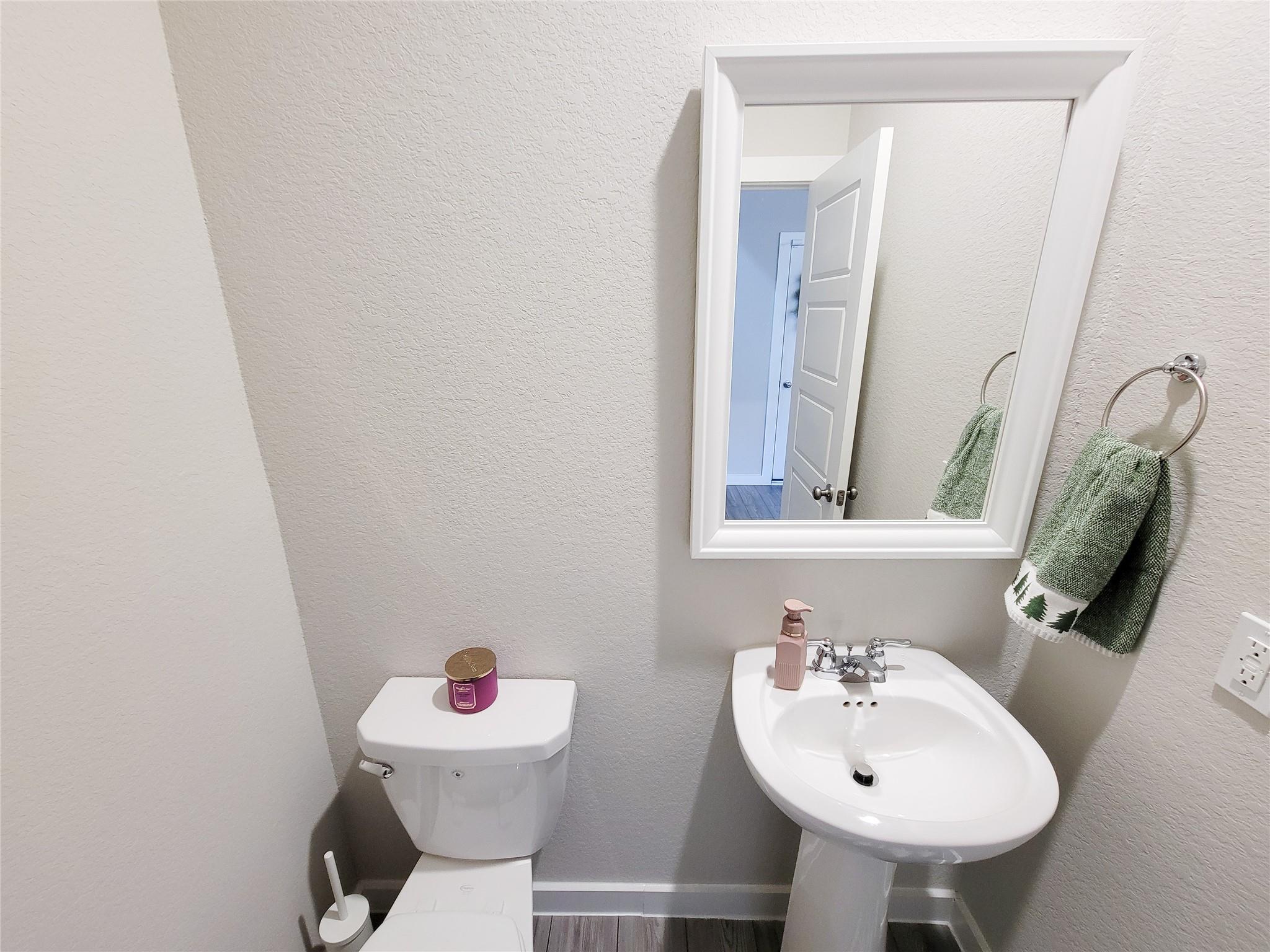 Bathroom with a pedestal sink, toilet, framed mirror, and green hand towels.