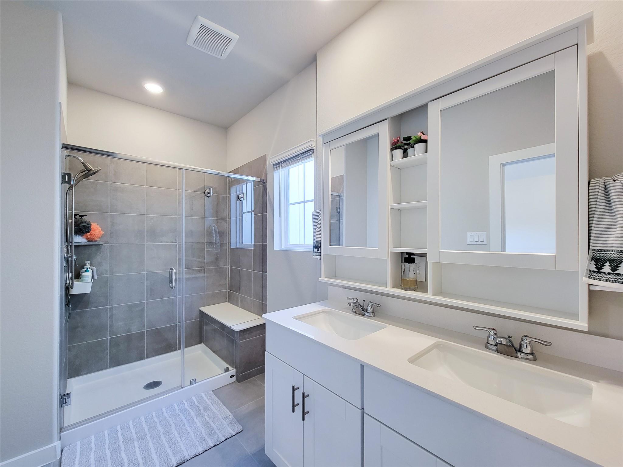 Bathroom with a gray tiled glass shower and white double-sink vanity.