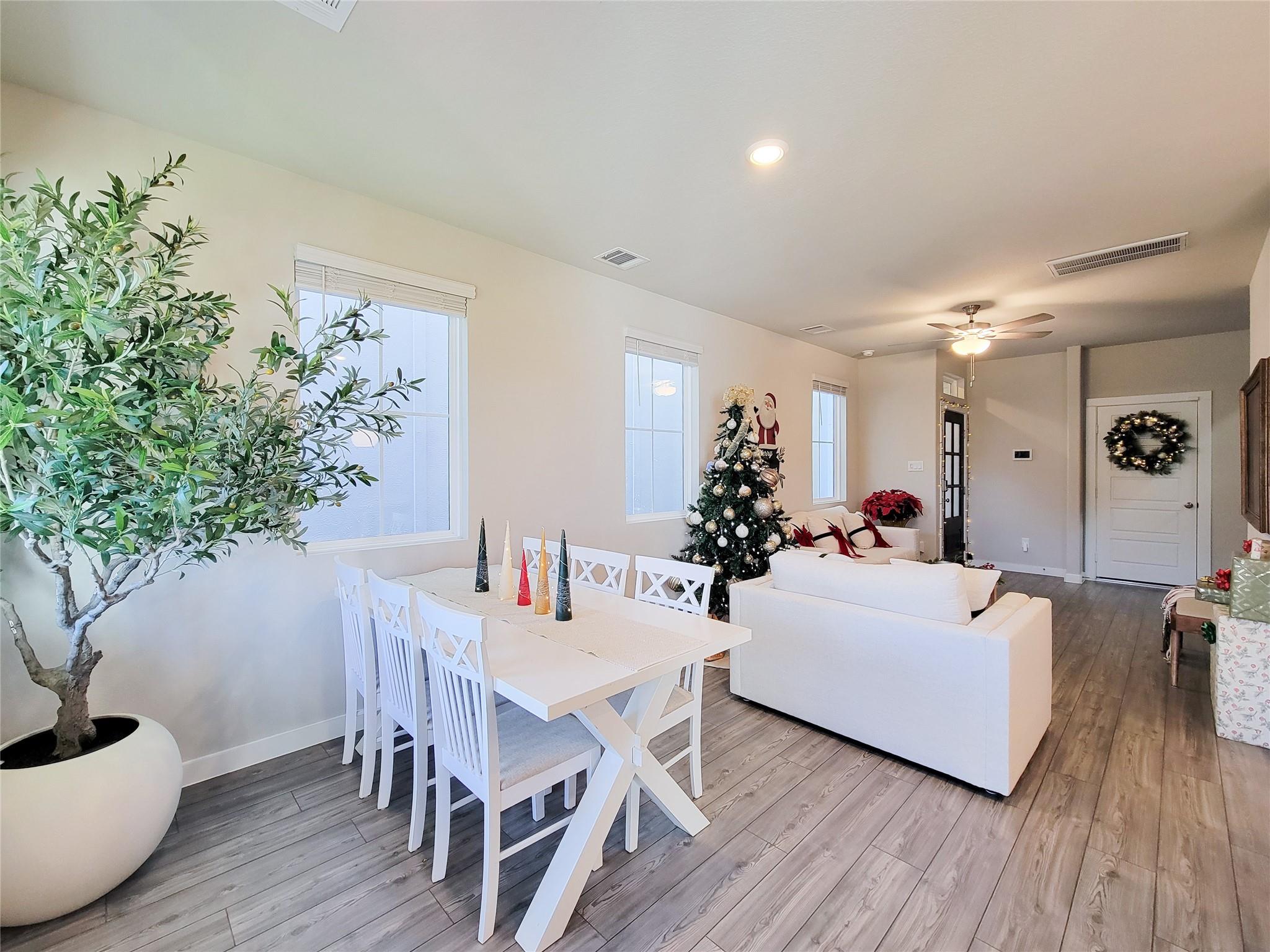 Open-plan living and dining room with white furniture, gray flooring, and a decorated Christmas tree.