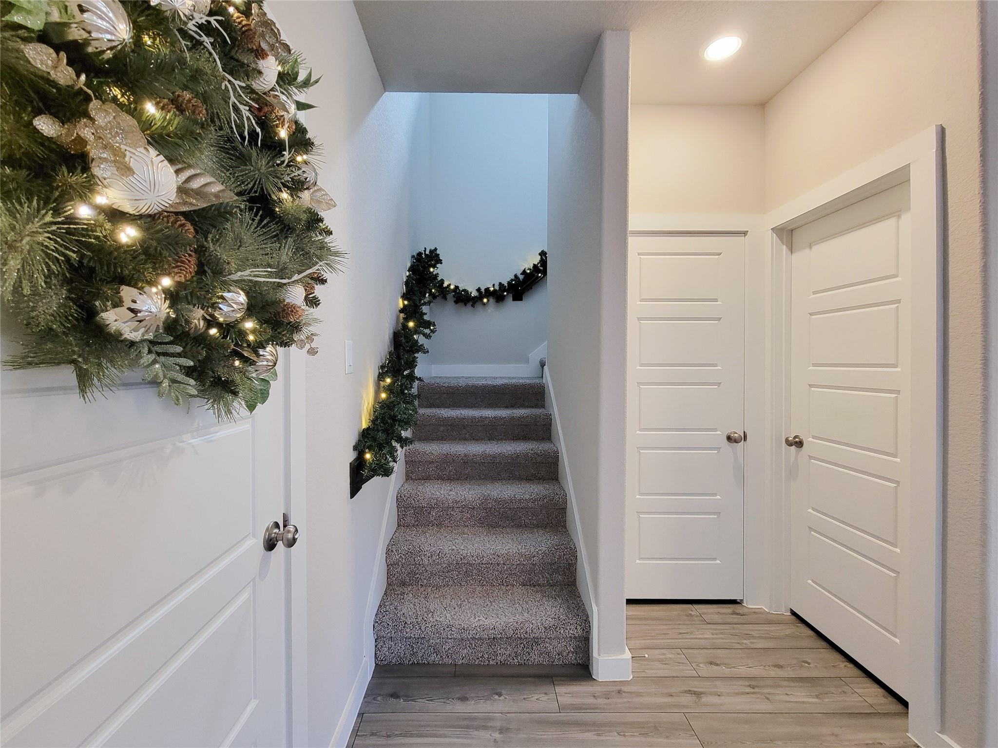 Carpeted staircase decorated with lit holiday garland, beside white paneled doors.