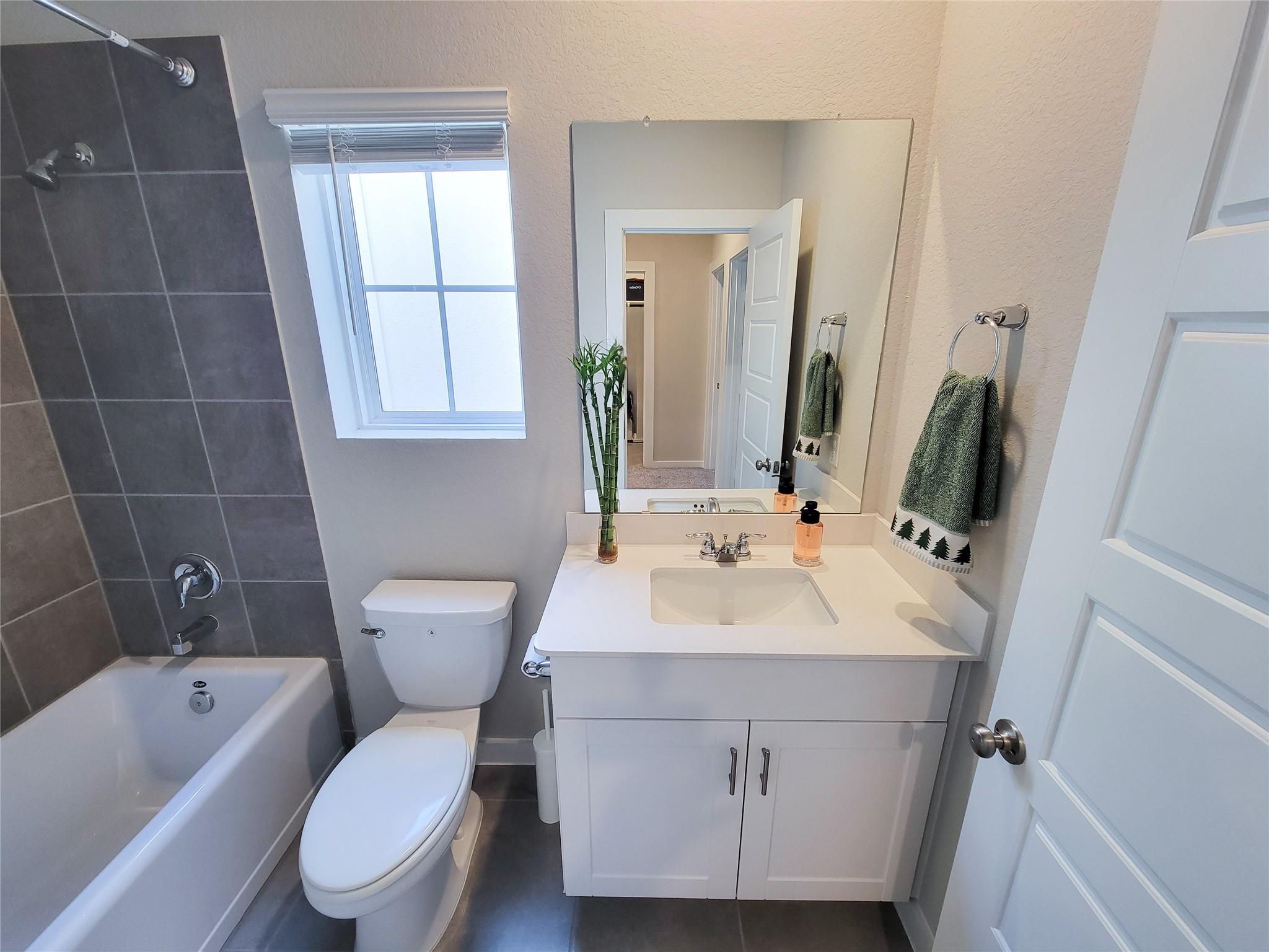 Bathroom with a gray-tiled tub and shower, white vanity, and window.