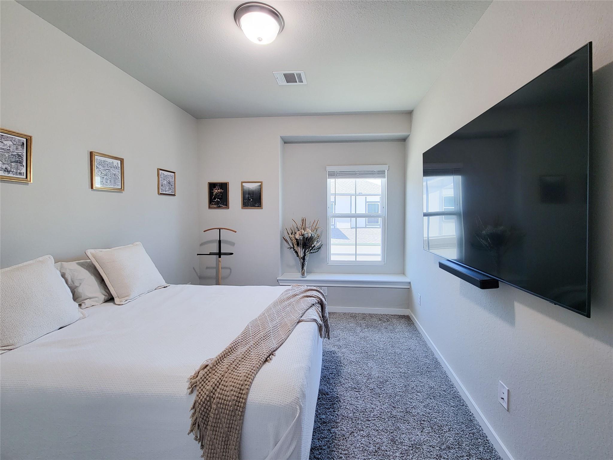 Furnished bedroom with a white bed, wall-mounted television, and window with blinds.
