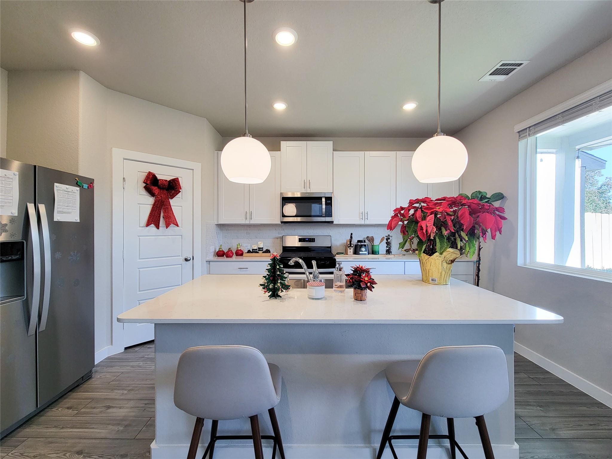 Modern kitchen with a large white island, pendant lights, and festive poinsettias.