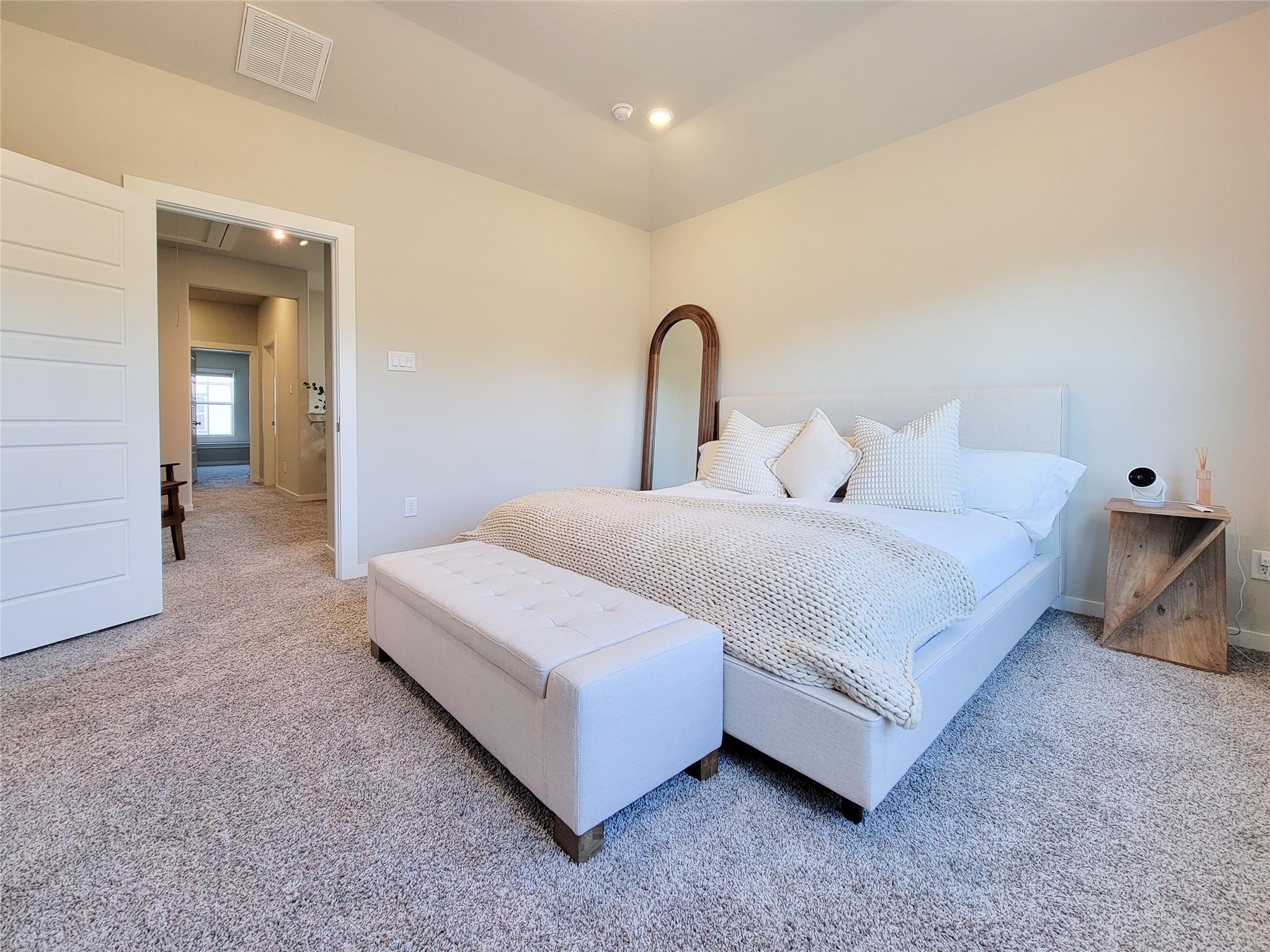 Staged bedroom with a white upholstered bed, textured bedding, a bench, and a tall arched mirror.
