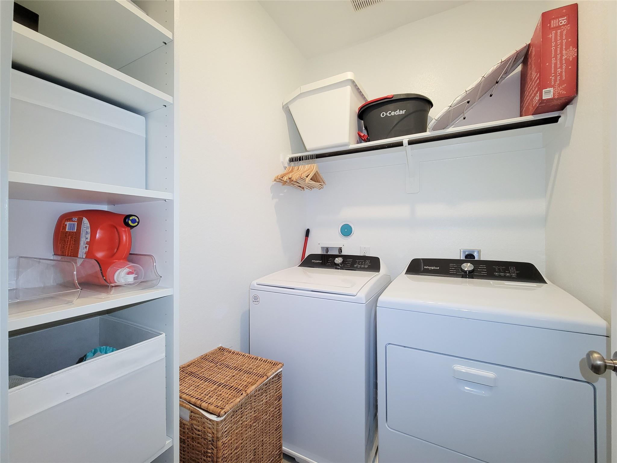 Laundry room with a washer and dryer, built-in shelving, overhead storage, and a wicker hamper.