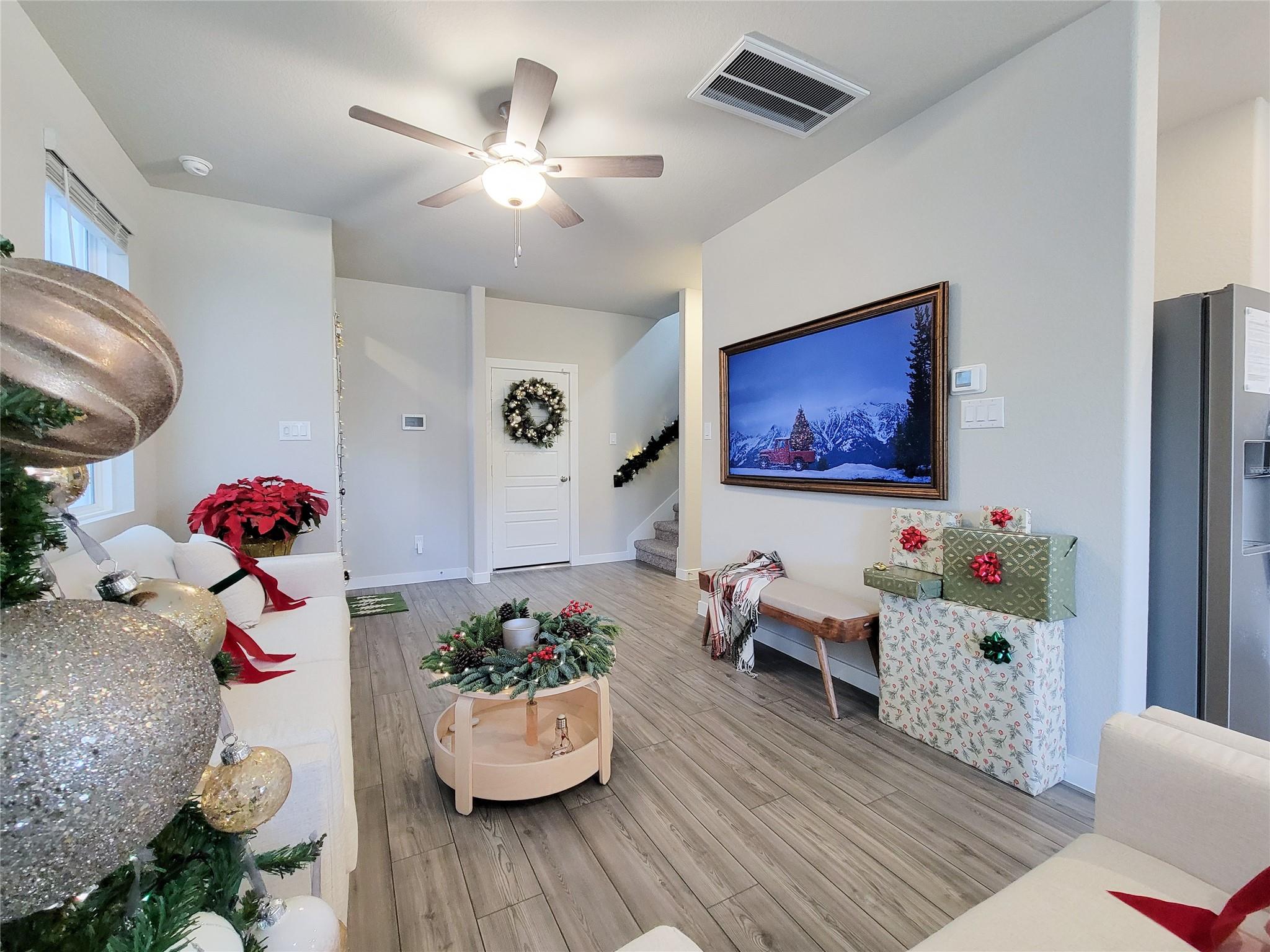 Living room with gray wood-look flooring, a ceiling fan, and Christmas decorations.