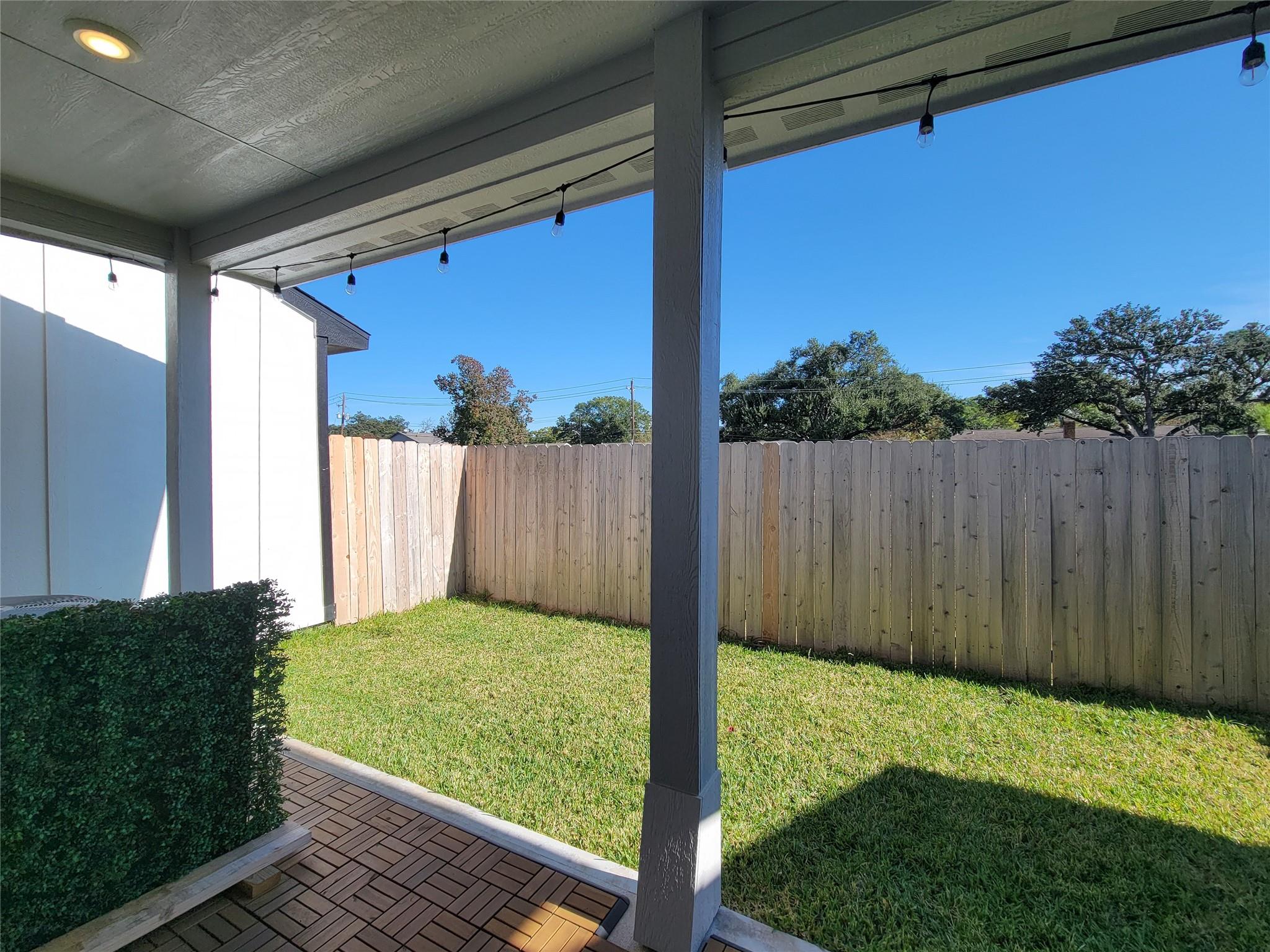Covered patio with string lights overlooking a fenced backyard lawn.