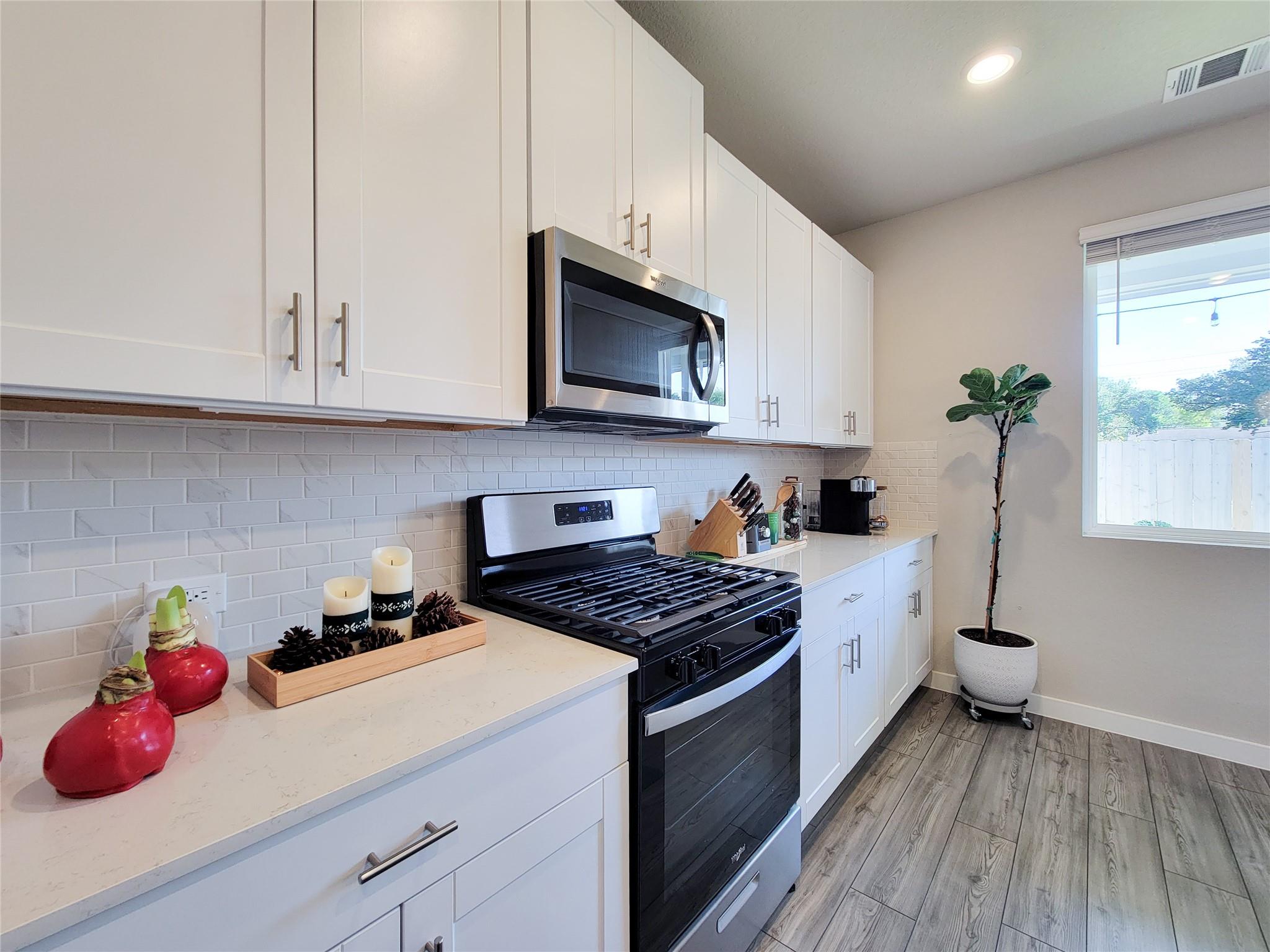 Bright kitchen with white cabinets, subway tile backsplash, and black range beside a window.