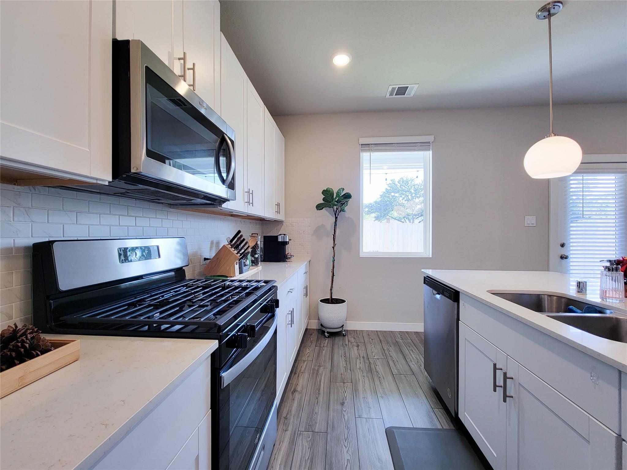 Modern kitchen with white cabinets, a large island sink, and stainless steel appliances.