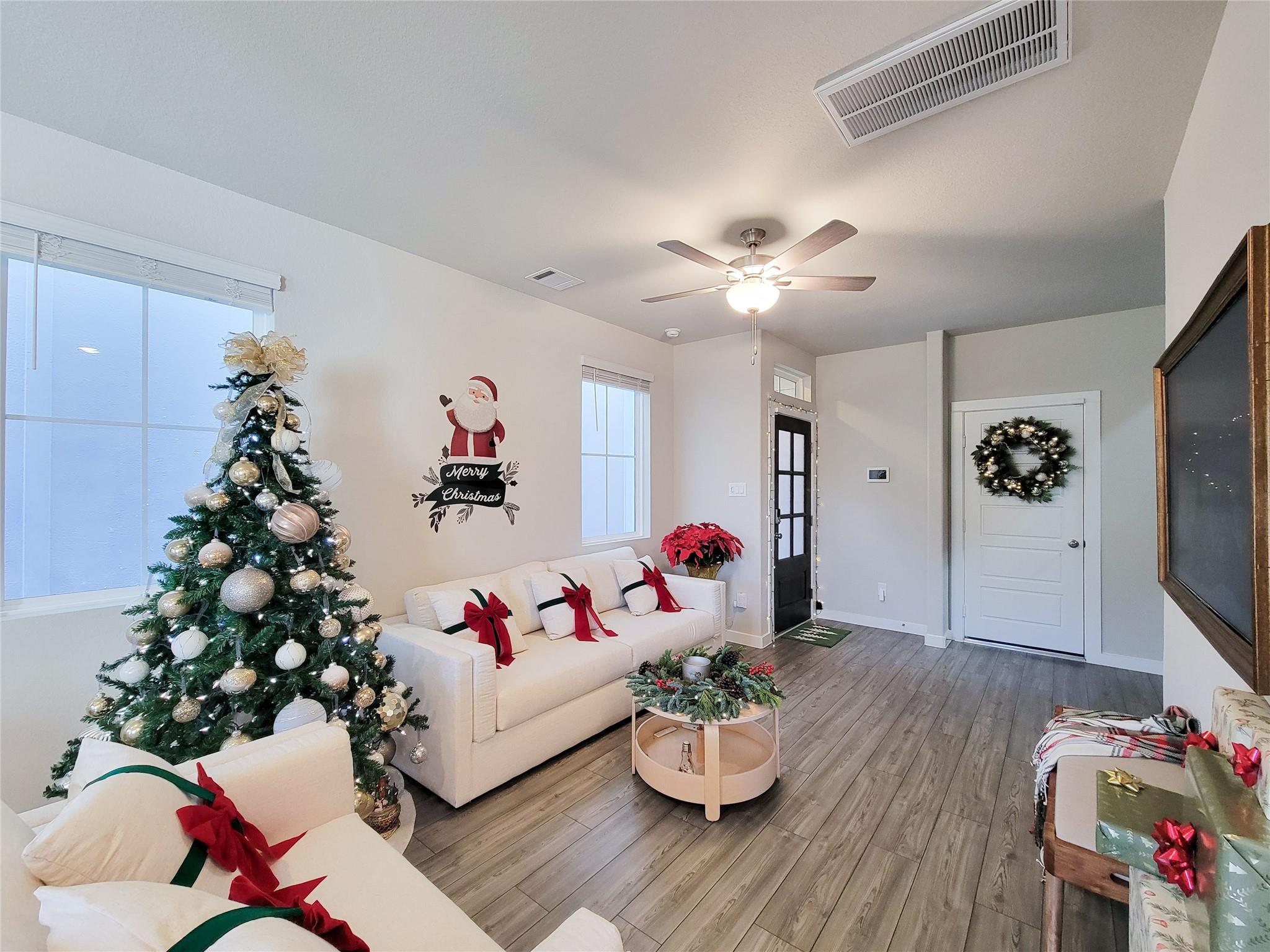 Living room with white sofas, a decorated Christmas tree, and seasonal gifts.