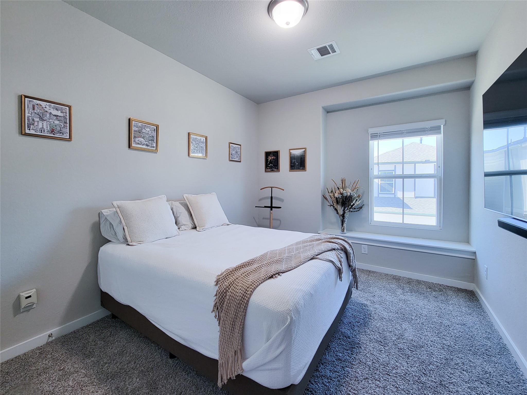 Bedroom with a white bed, textured throw, framed art, and a large window.