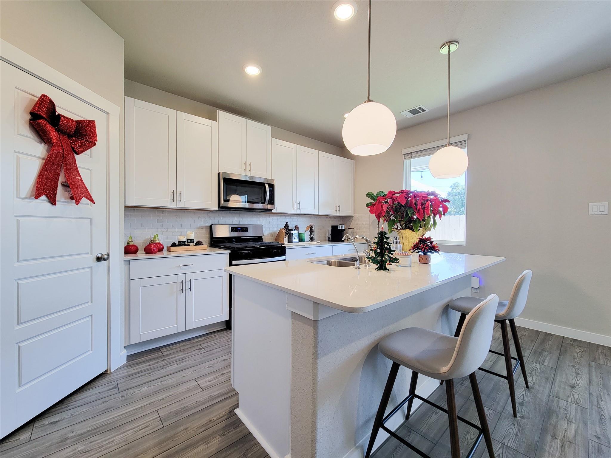 Bright kitchen with white cabinets, stainless appliances, and a large island with bar seating.