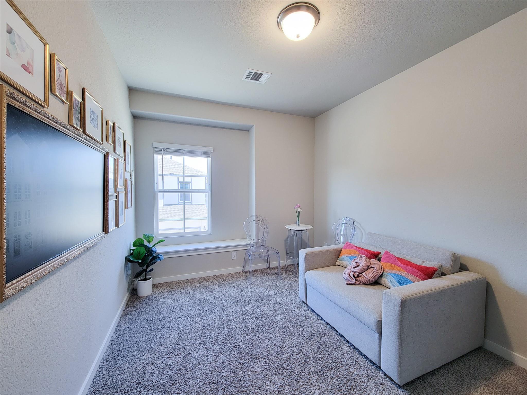 Sitting room with a gray sofa, colorful pillows, clear chairs, and framed artwork.