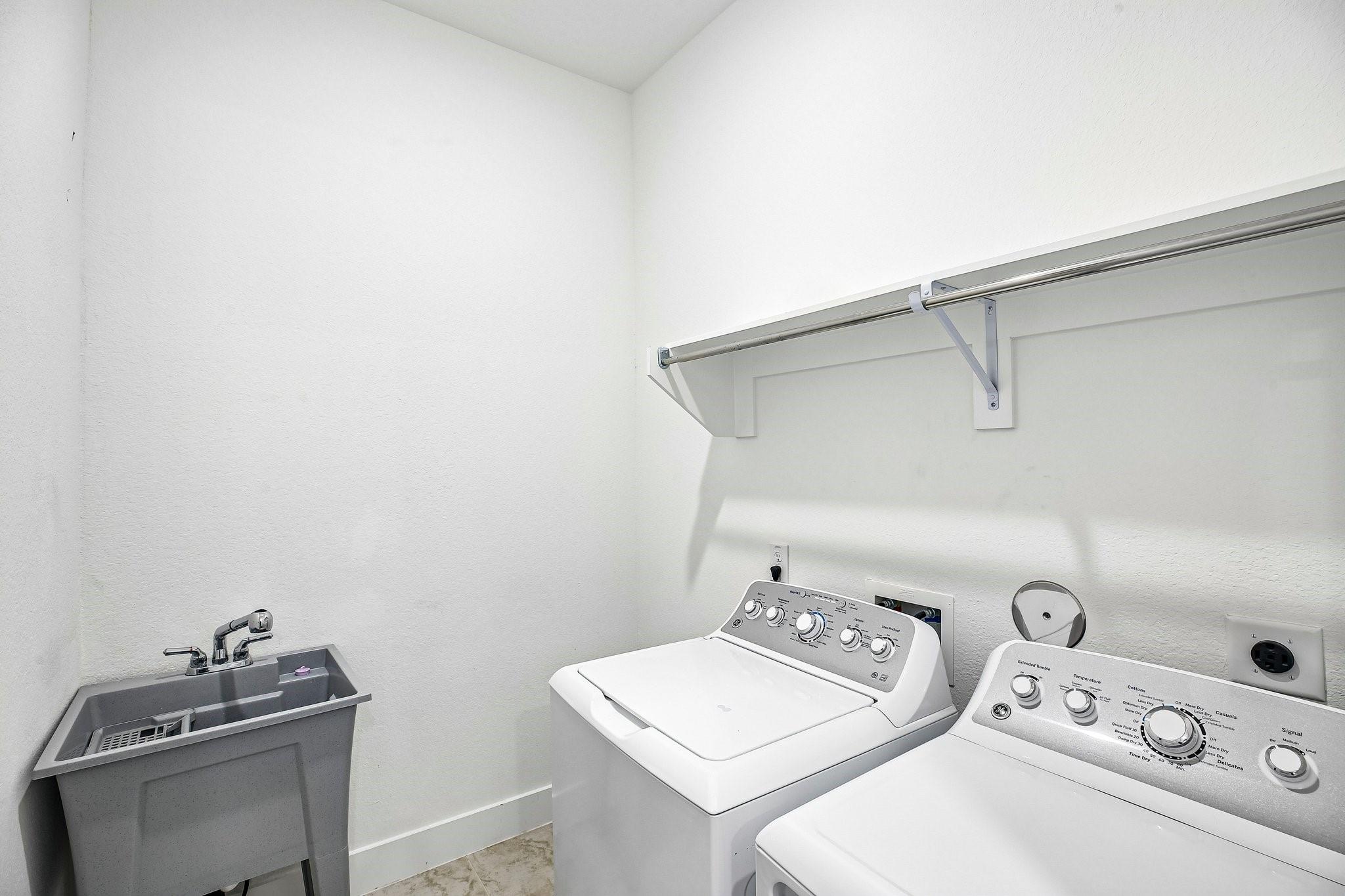 Laundry room with a washer and dryer, deep utility sink, and wall-mounted shelf and hanging rod.