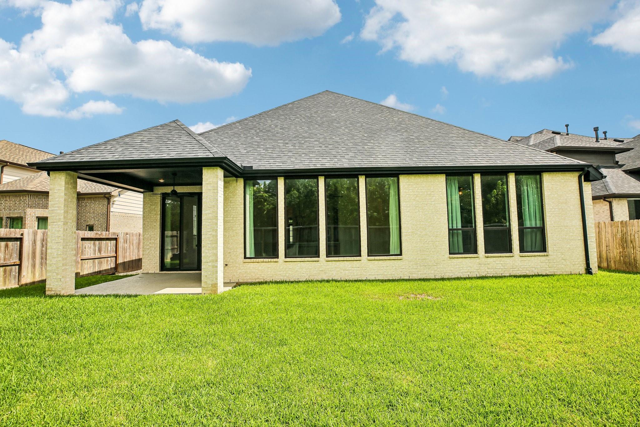Rear of a brick house with tall windows and a covered patio overlooking a wide lawn.