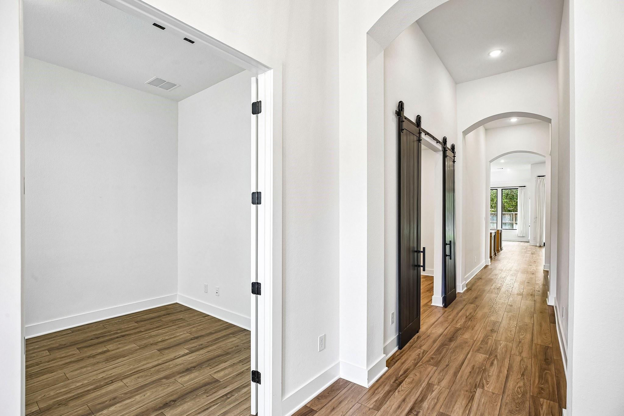 Wood-look tile hallway with arched openings and dark barn doors beside an empty room.