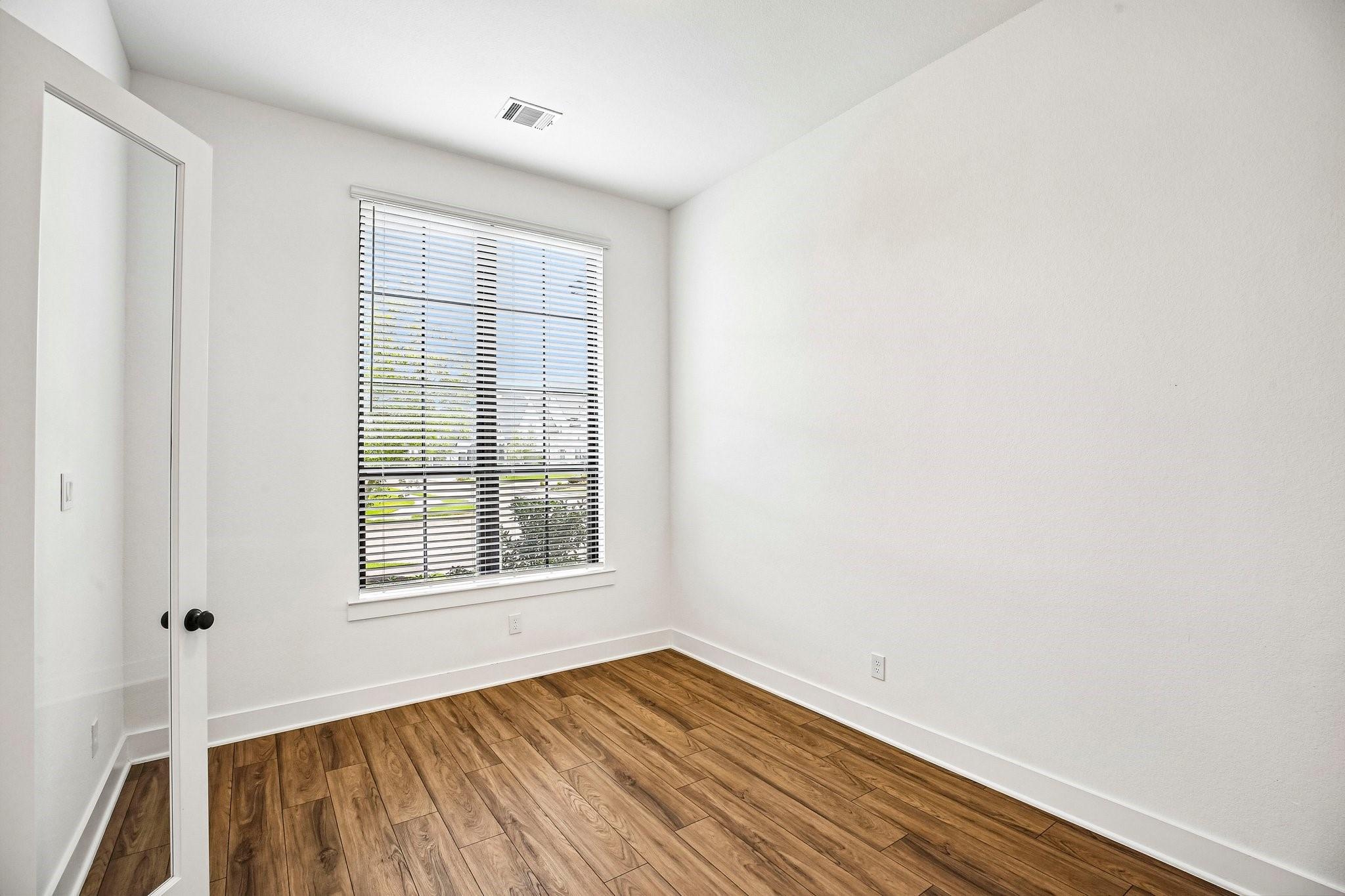Empty room with wood-look flooring, white walls, and a window with horizontal blinds.