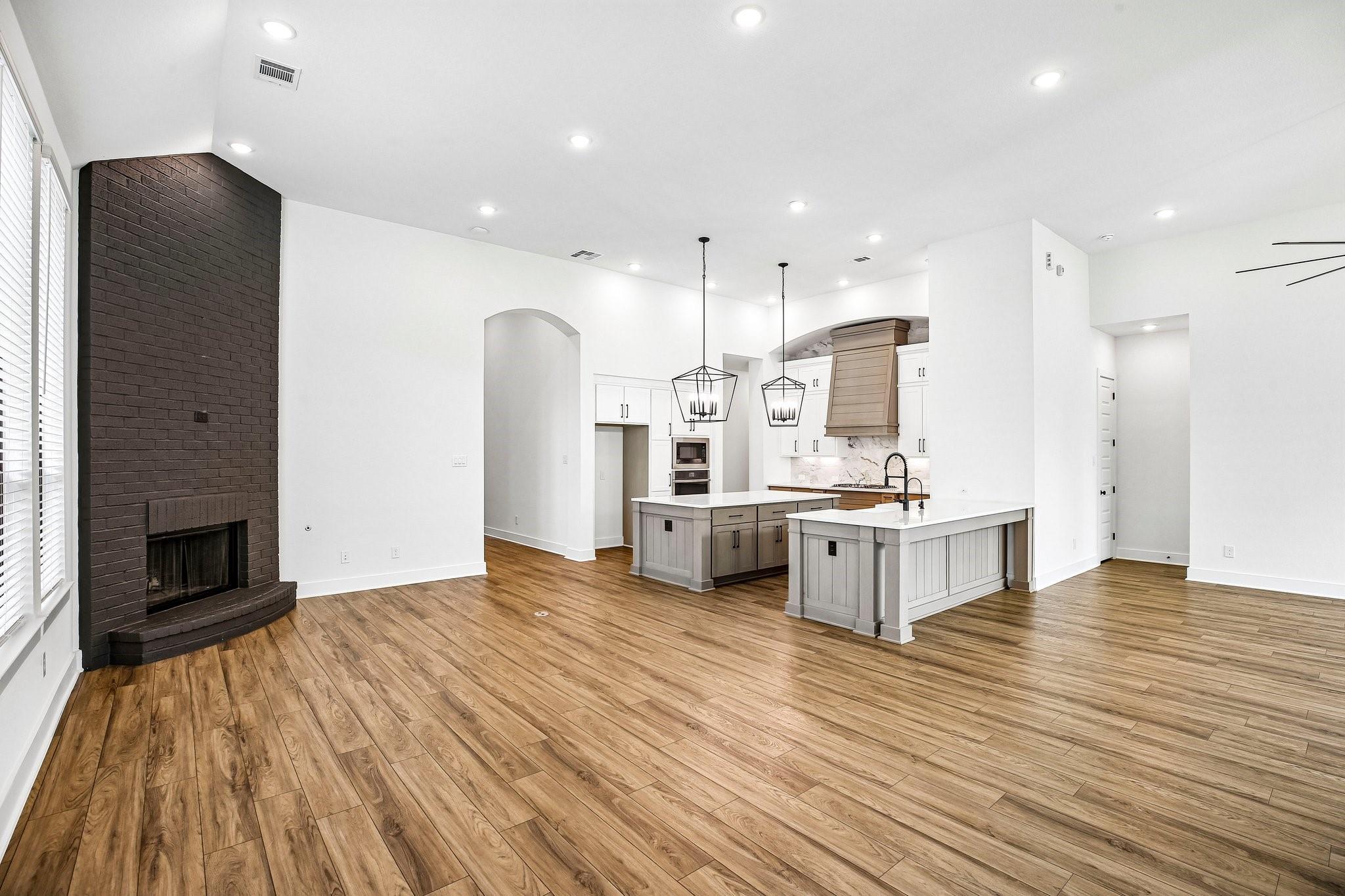 Open-plan kitchen and living area with a dark brick fireplace, wood floors, and two islands.