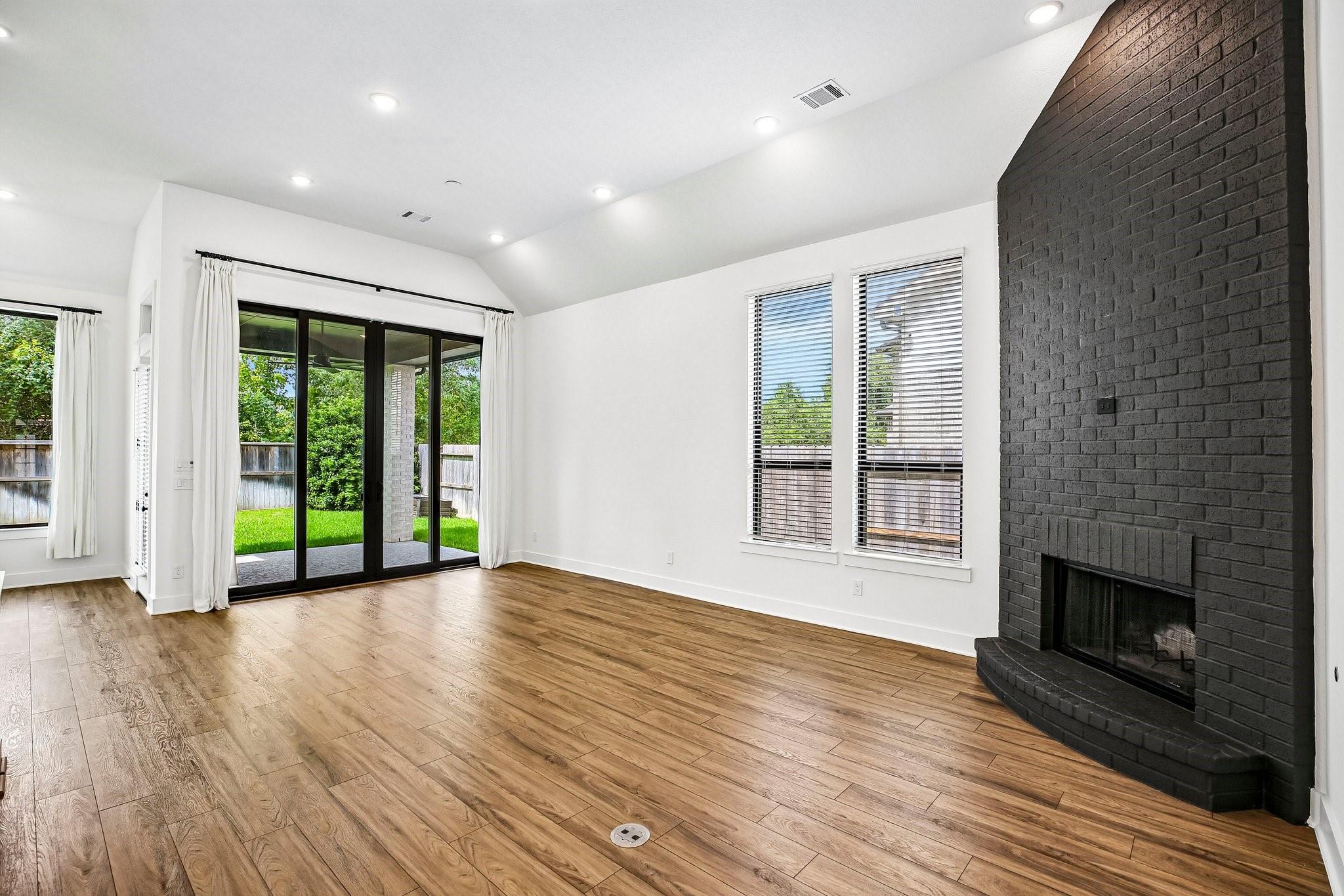 Empty living room with wood floors, a black brick fireplace, and sliding doors to the backyard.