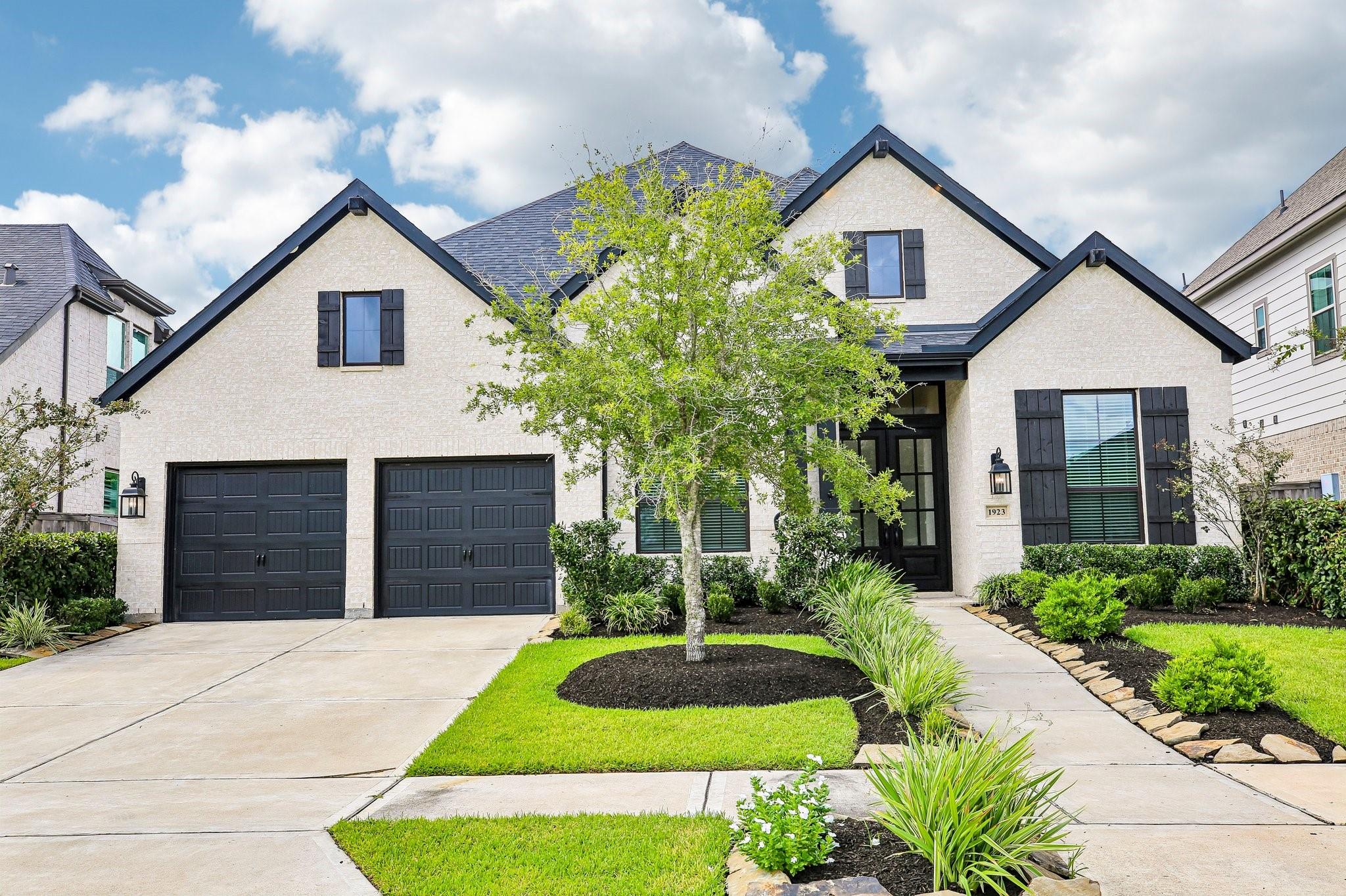 Light brick house with black gables, two dark garage doors, and a landscaped front lawn.
