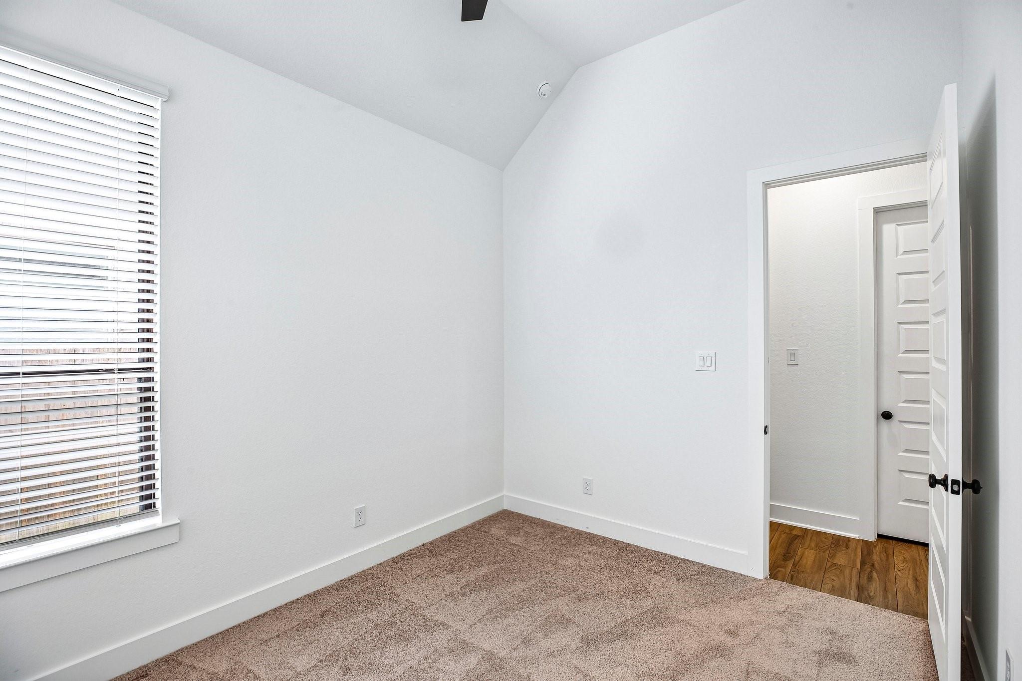 Empty bedroom with beige carpet, a high sloped ceiling, and a window with white blinds.