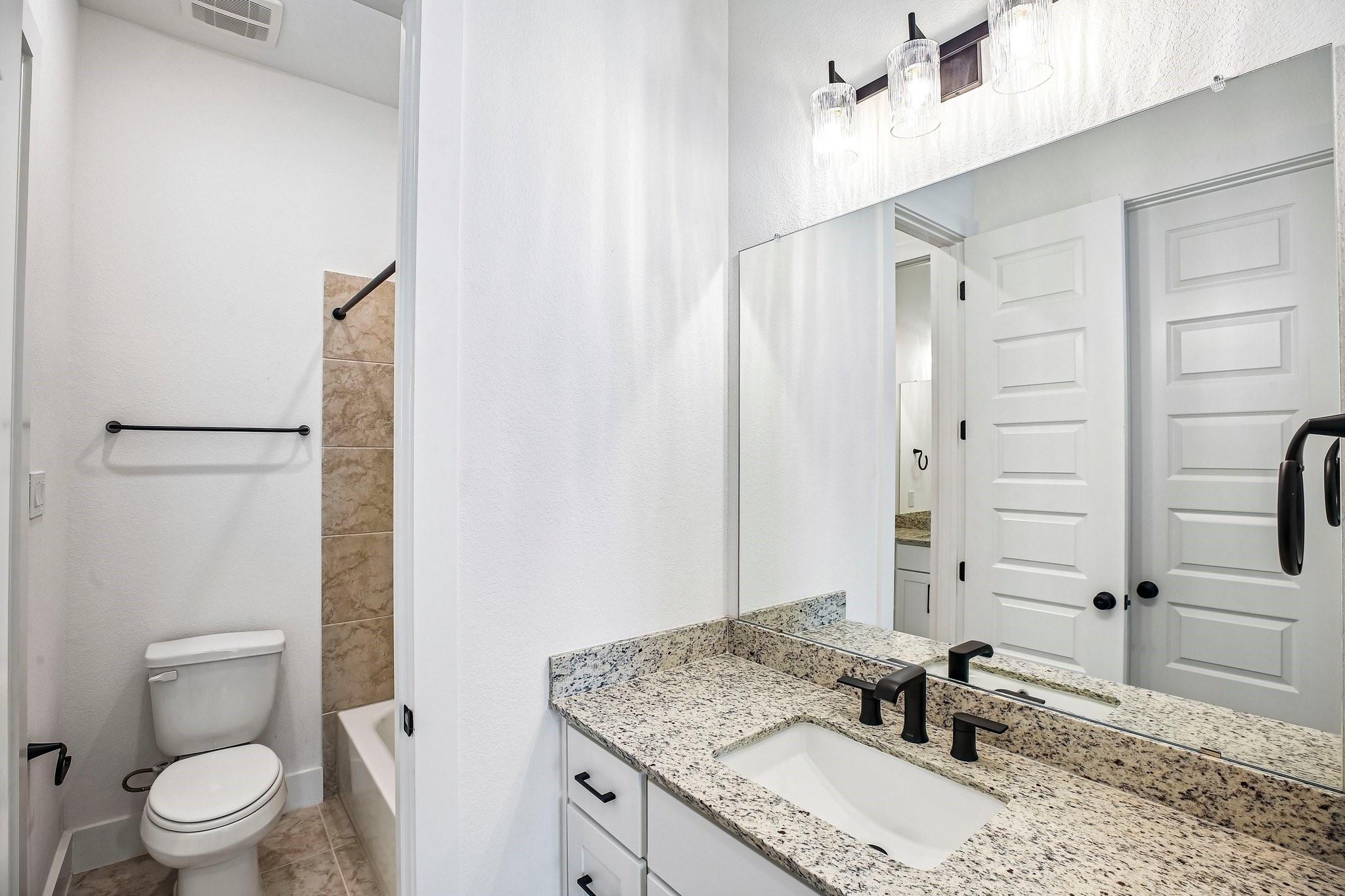 Bathroom with a granite vanity and large mirror beside a tiled tub and shower.