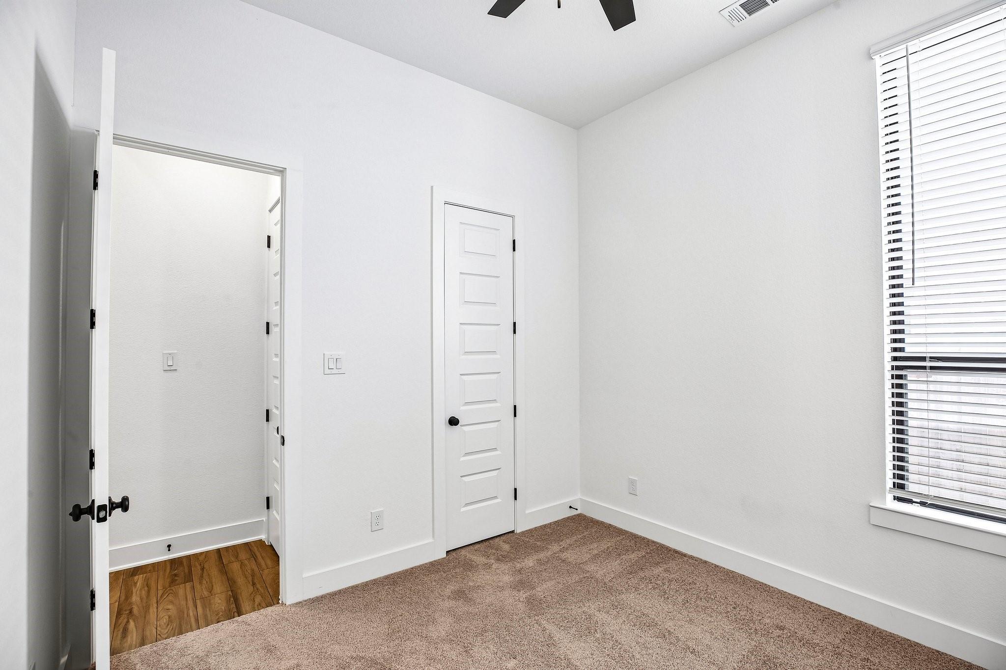 Empty bedroom with beige carpet, a ceiling fan, and a window with white blinds.