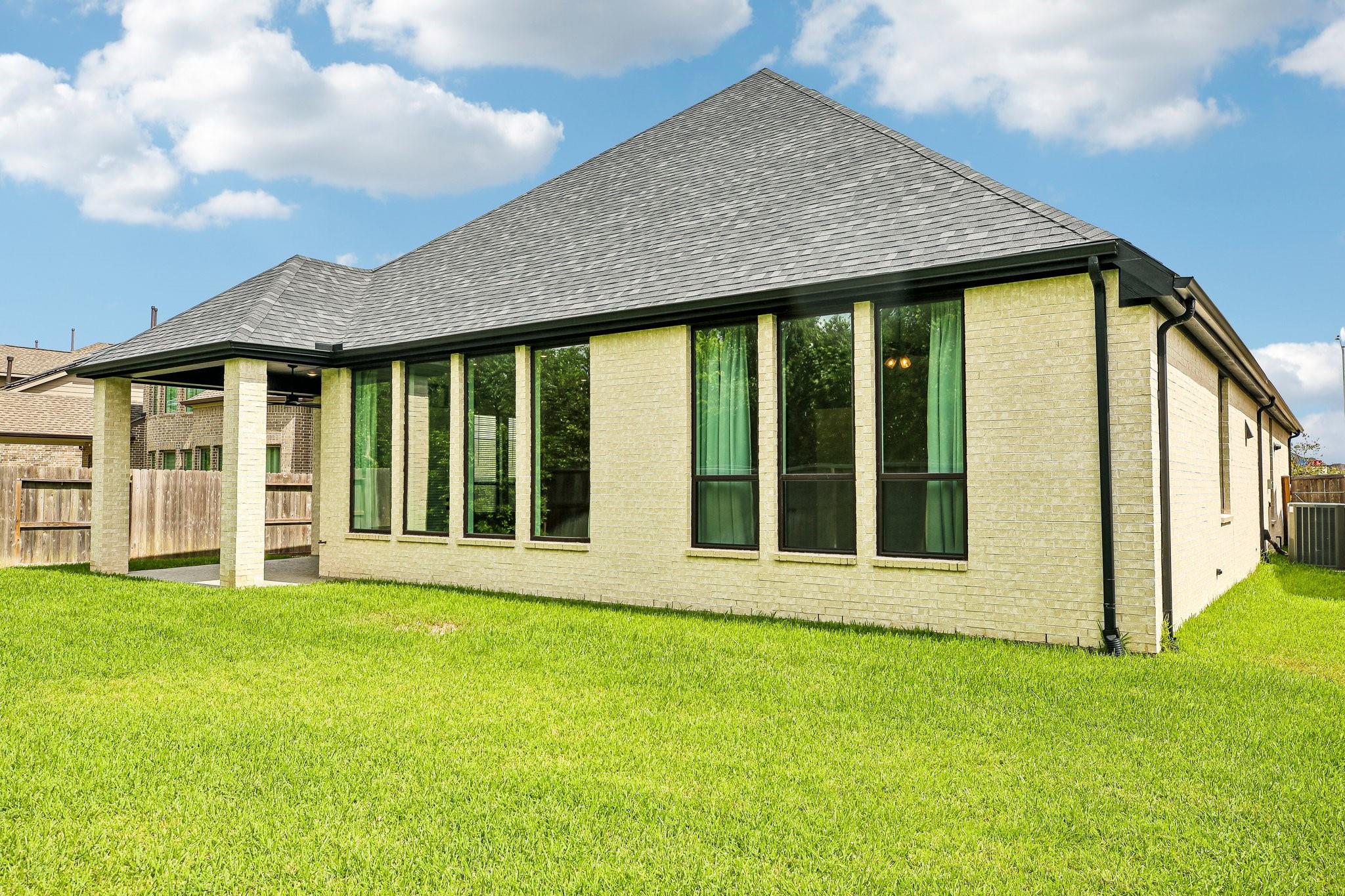 Light brick home with a covered patio, tall windows, and a broad green lawn.