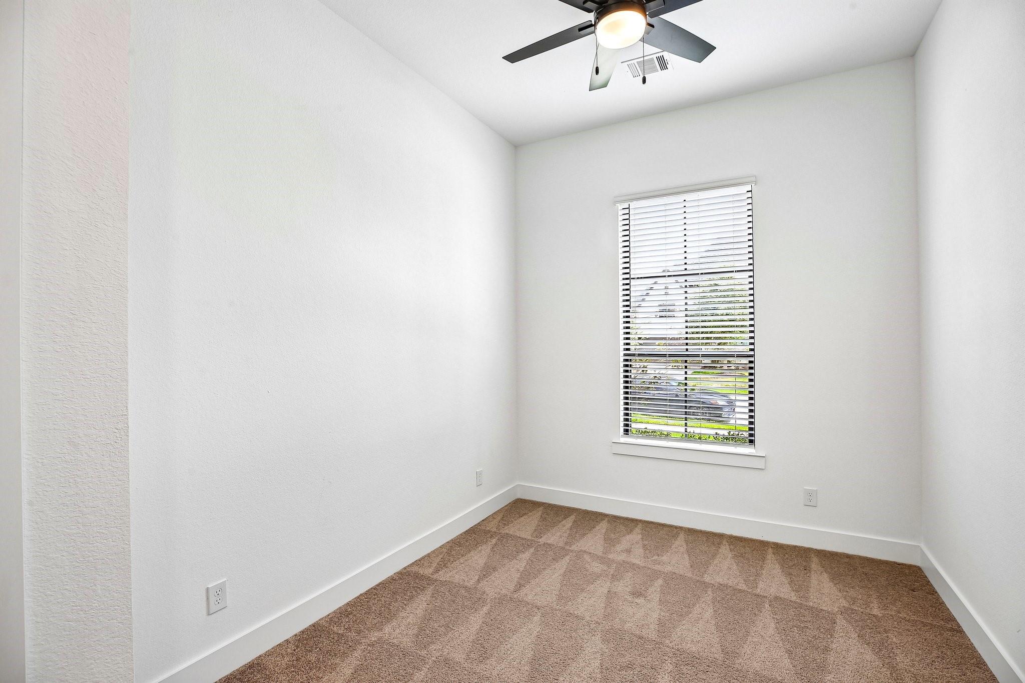 Empty bedroom with brown carpet, a window with white blinds, and a ceiling fan.
