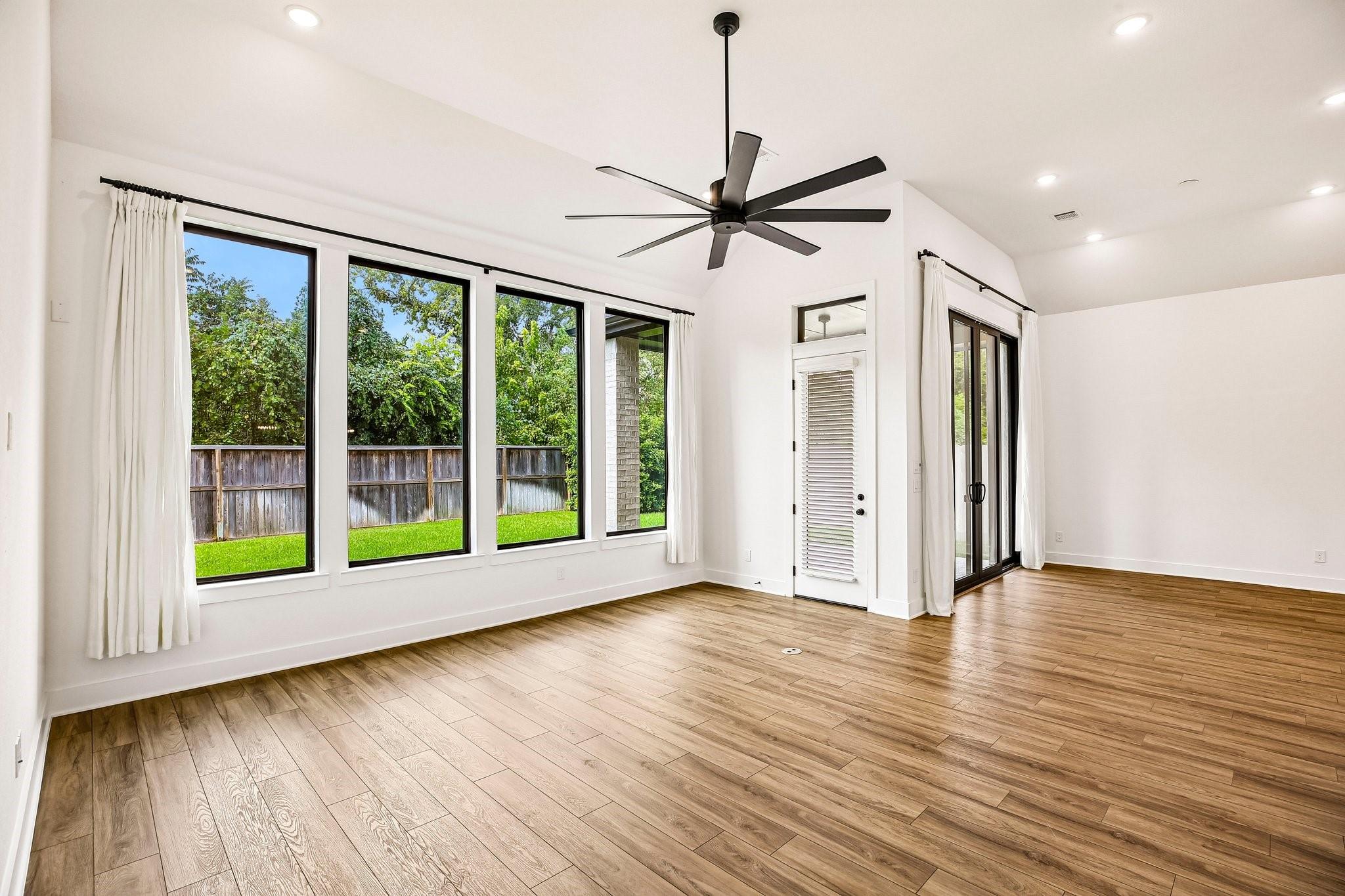 Vacant living room with large yard-facing windows, wood-look floors, and sliding glass doors.