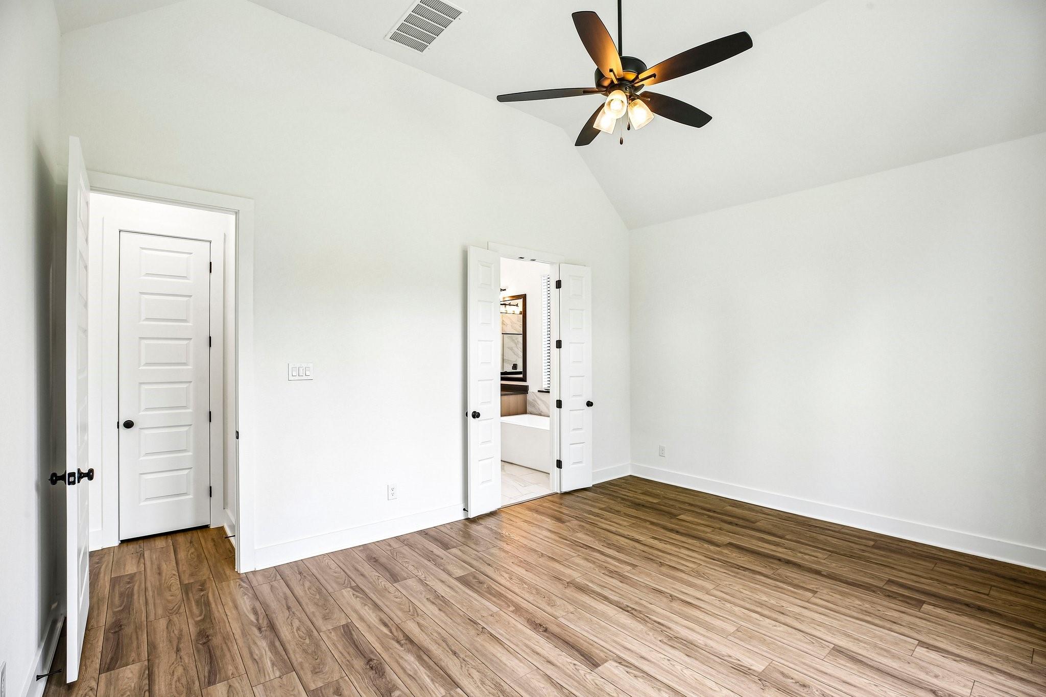 Vacant room with wood-look flooring, a vaulted ceiling, and open doors to an adjoining bathroom.