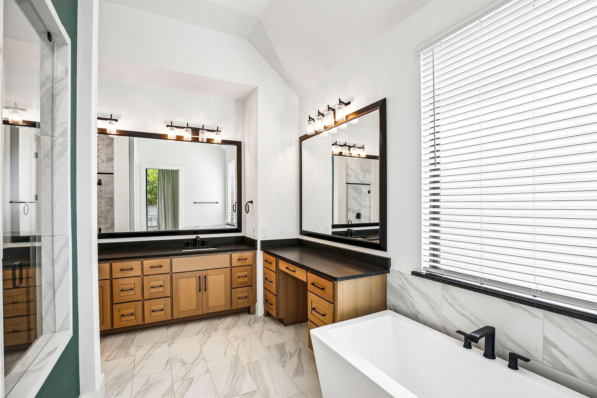 Bathroom with a freestanding tub, glass shower, marble-look tile, and warm wood vanities.