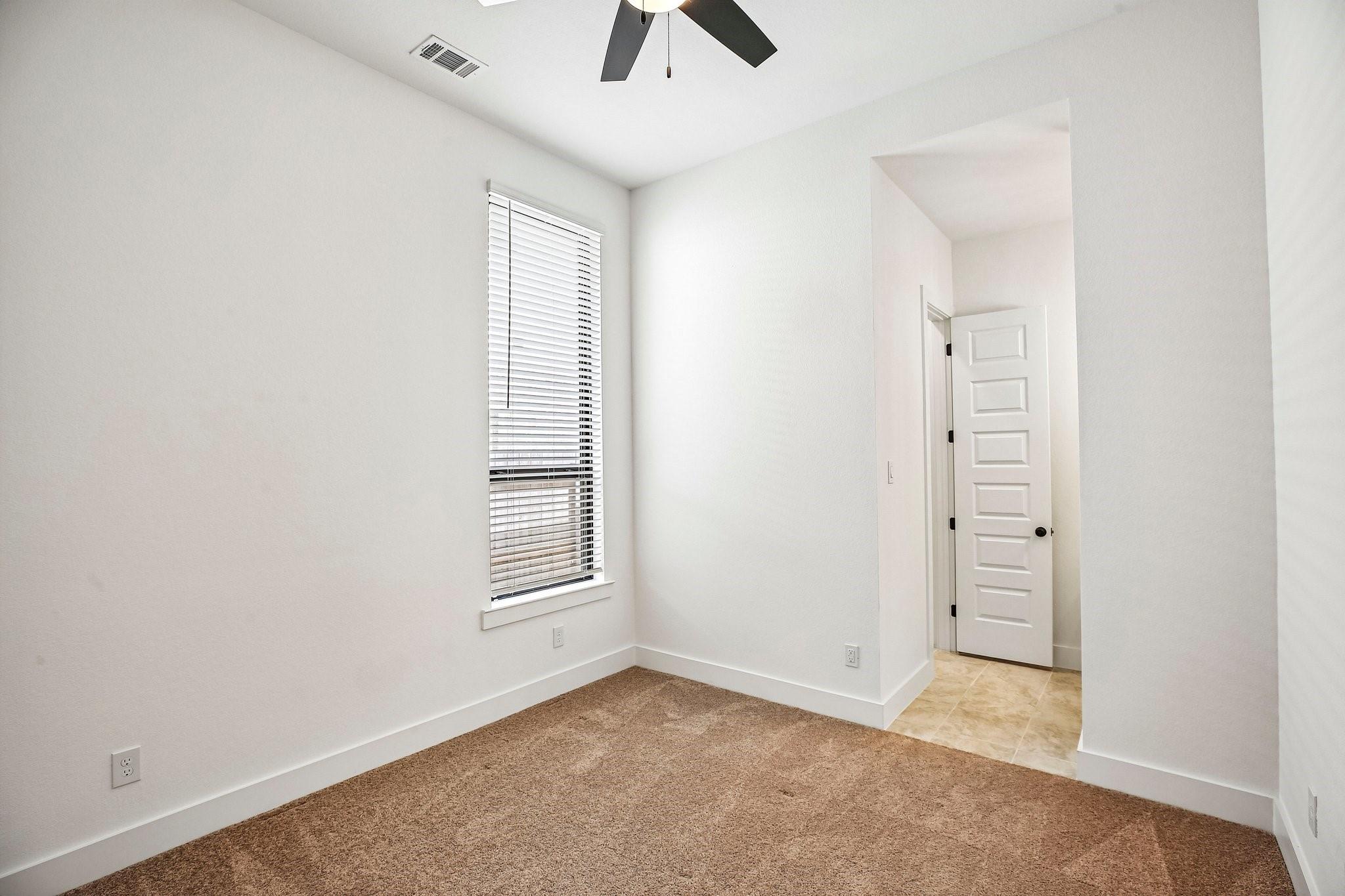 Empty bedroom with brown carpet, window blinds, and an open doorway to a tiled hall.