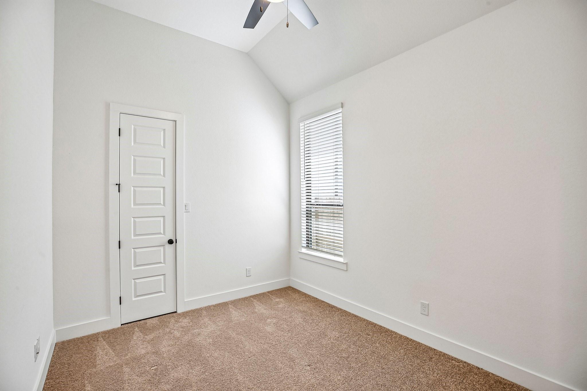 Empty carpeted room with a paneled door, tall window with blinds, and sloped ceiling.
