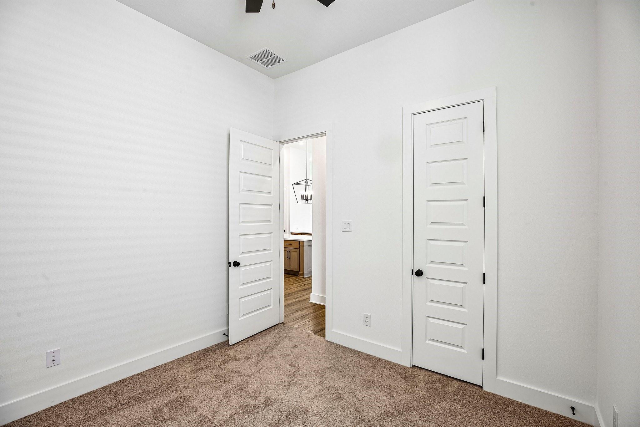 Empty carpeted bedroom with white paneled doors and a ceiling fan.