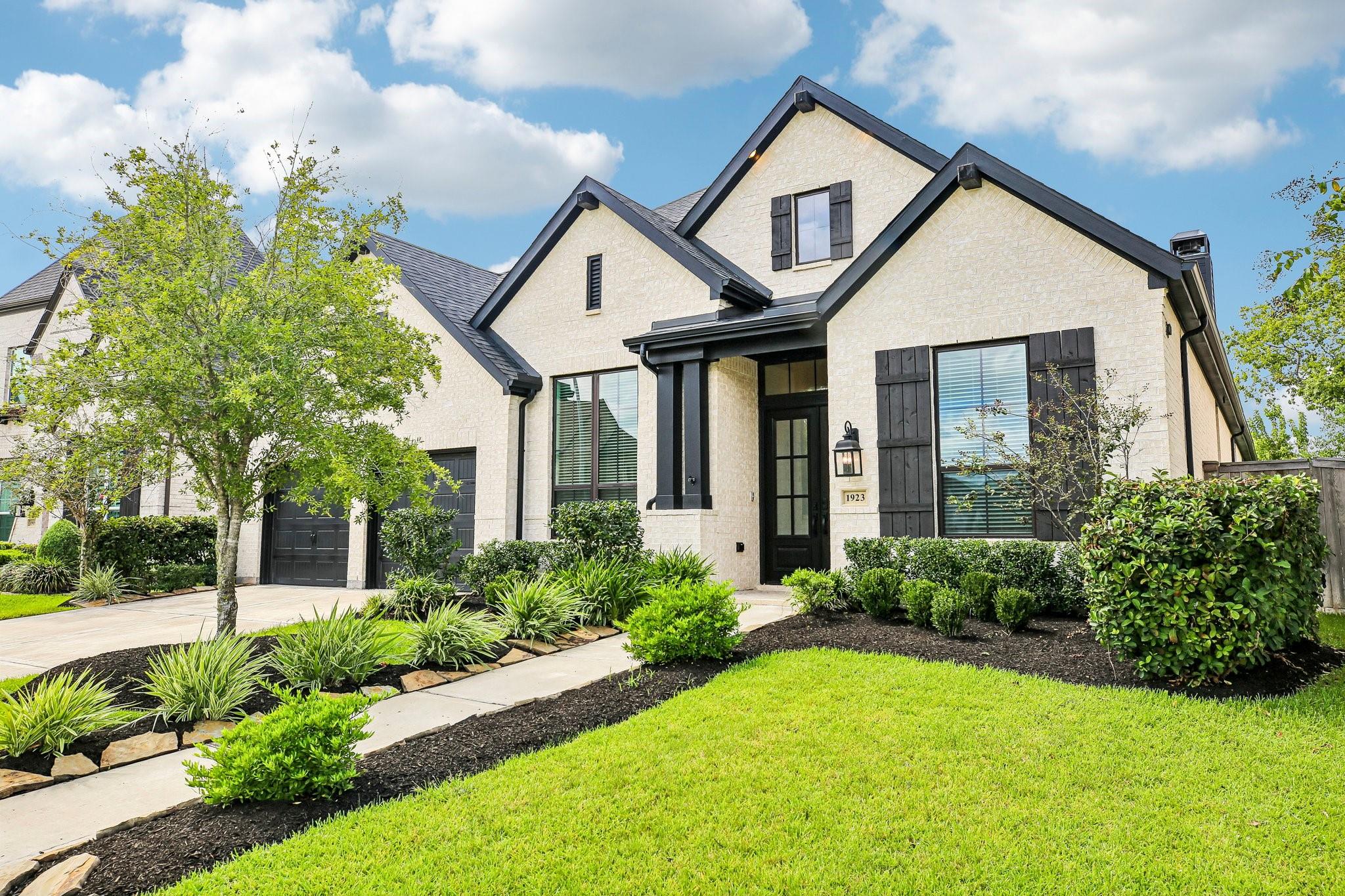 Light brick two-story home with dark gables, black shutters, and a landscaped front walkway.