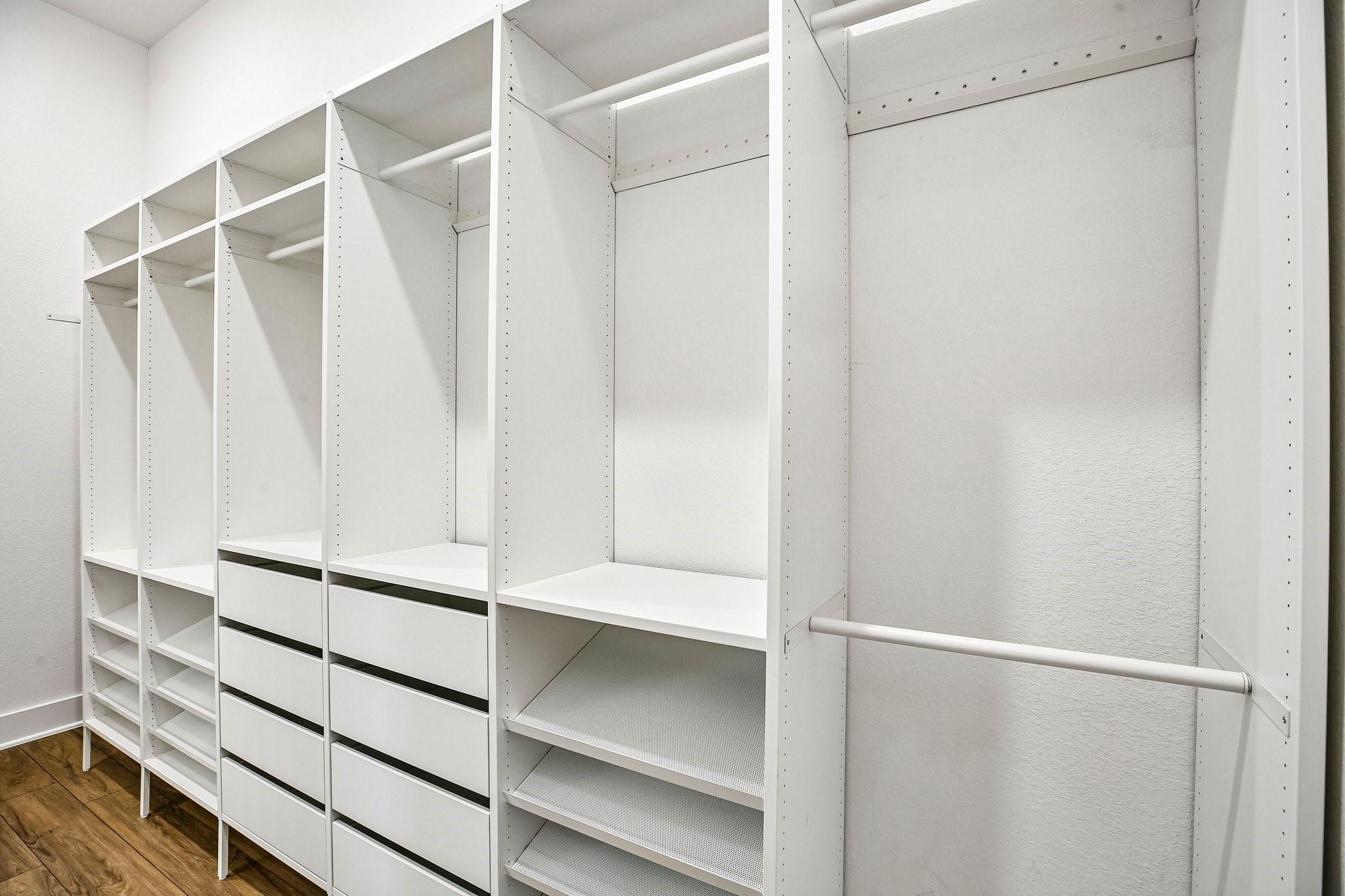 Walk-in closet with white built-in shelves, drawers, and hanging rods.