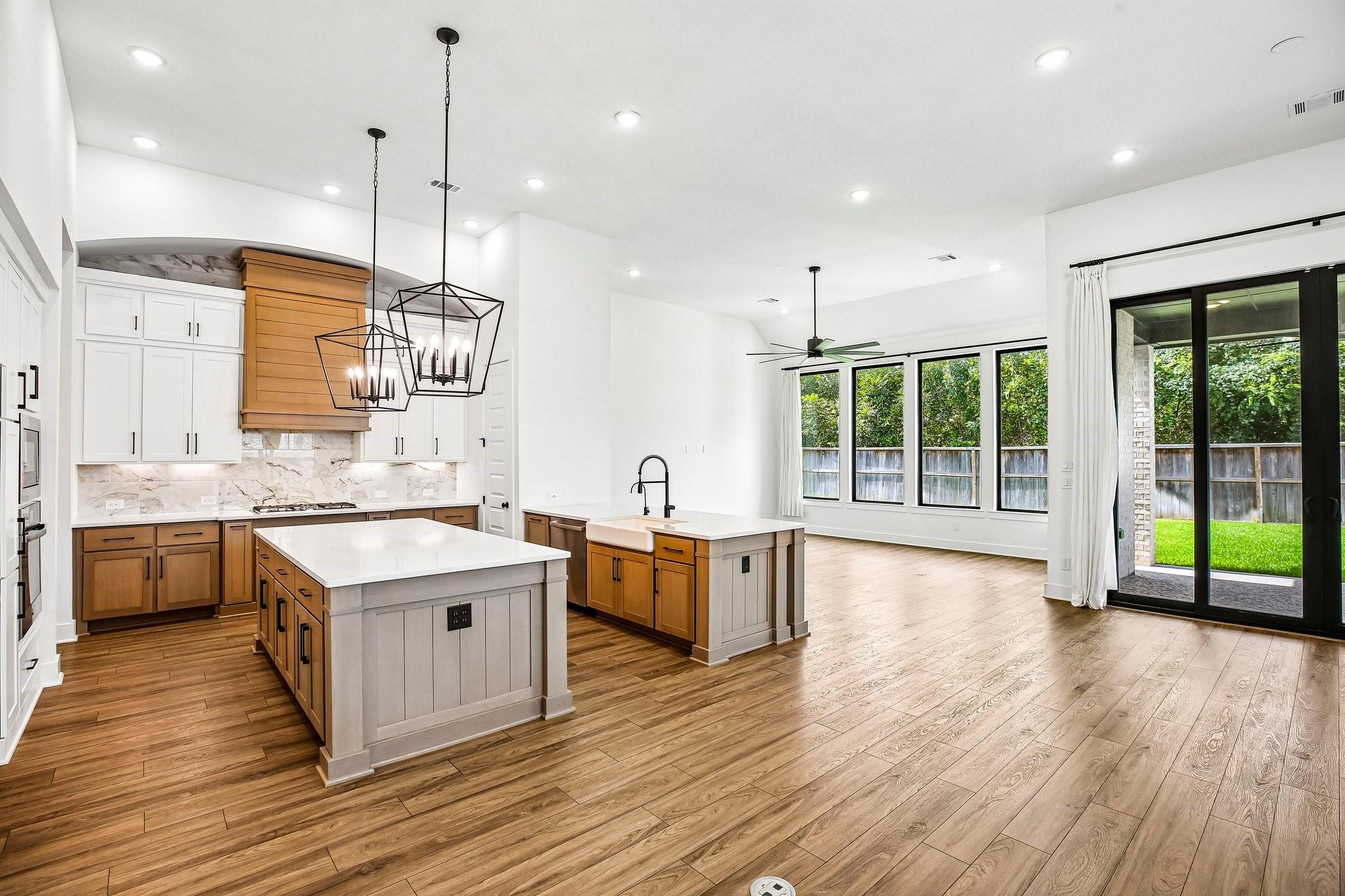 Open kitchen with two islands, warm wood cabinetry, and black-framed windows overlooking the yard.