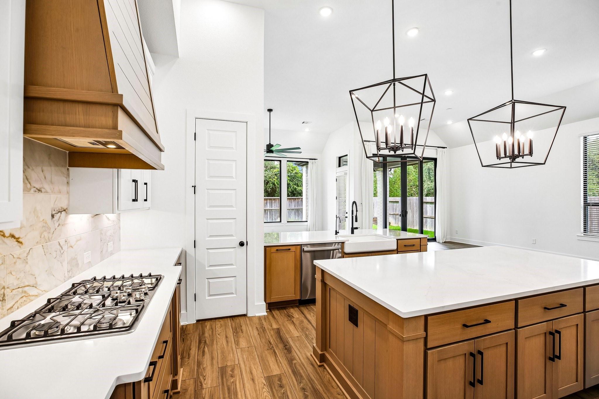 Modern kitchen with a wood-cabinet island, marble-look backsplash, and geometric pendant lights.