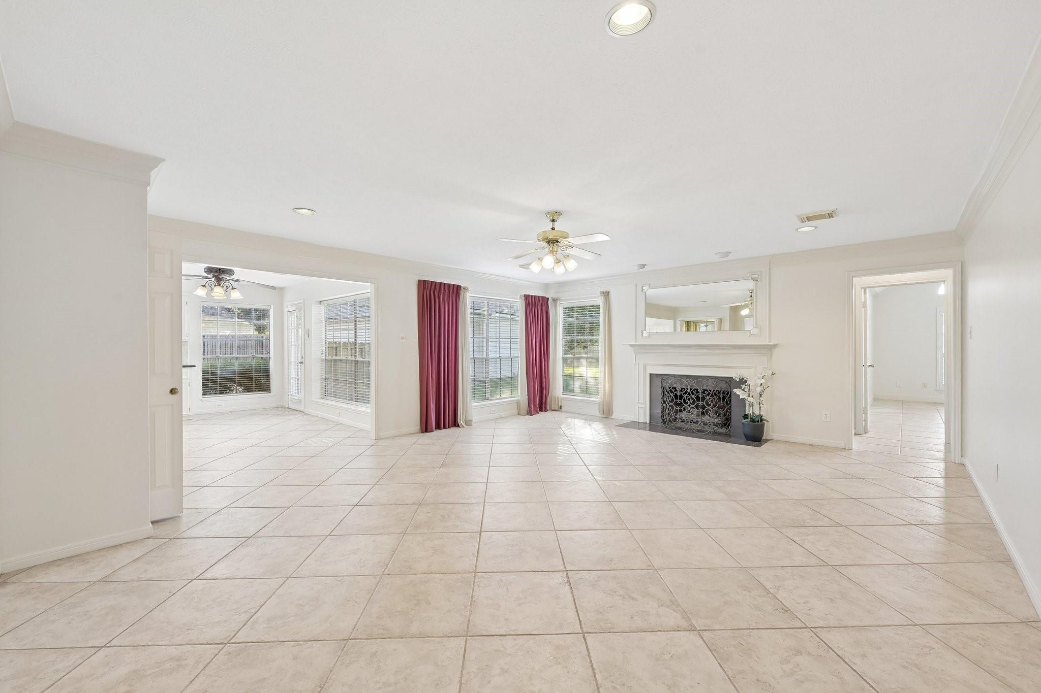 Empty living room with a white fireplace, burgundy curtains, and large tile floors.